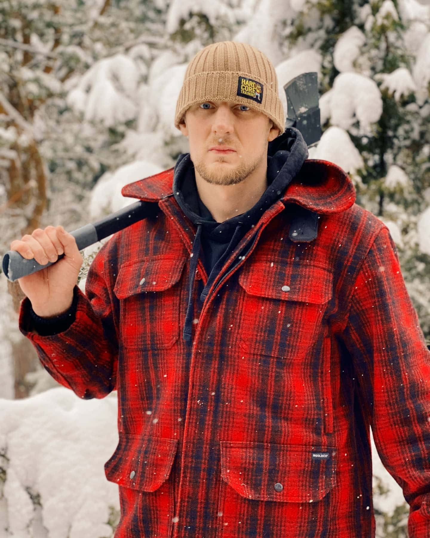 穿著紅色格仔外套的男人在雪地森林中拿著斧頭。