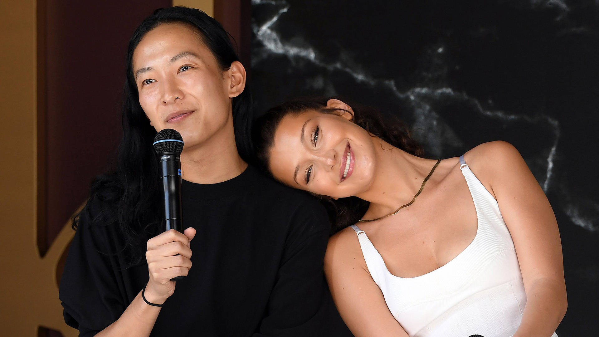 兩名女子，一人手持麥克風在室內大理石牆附近微笑