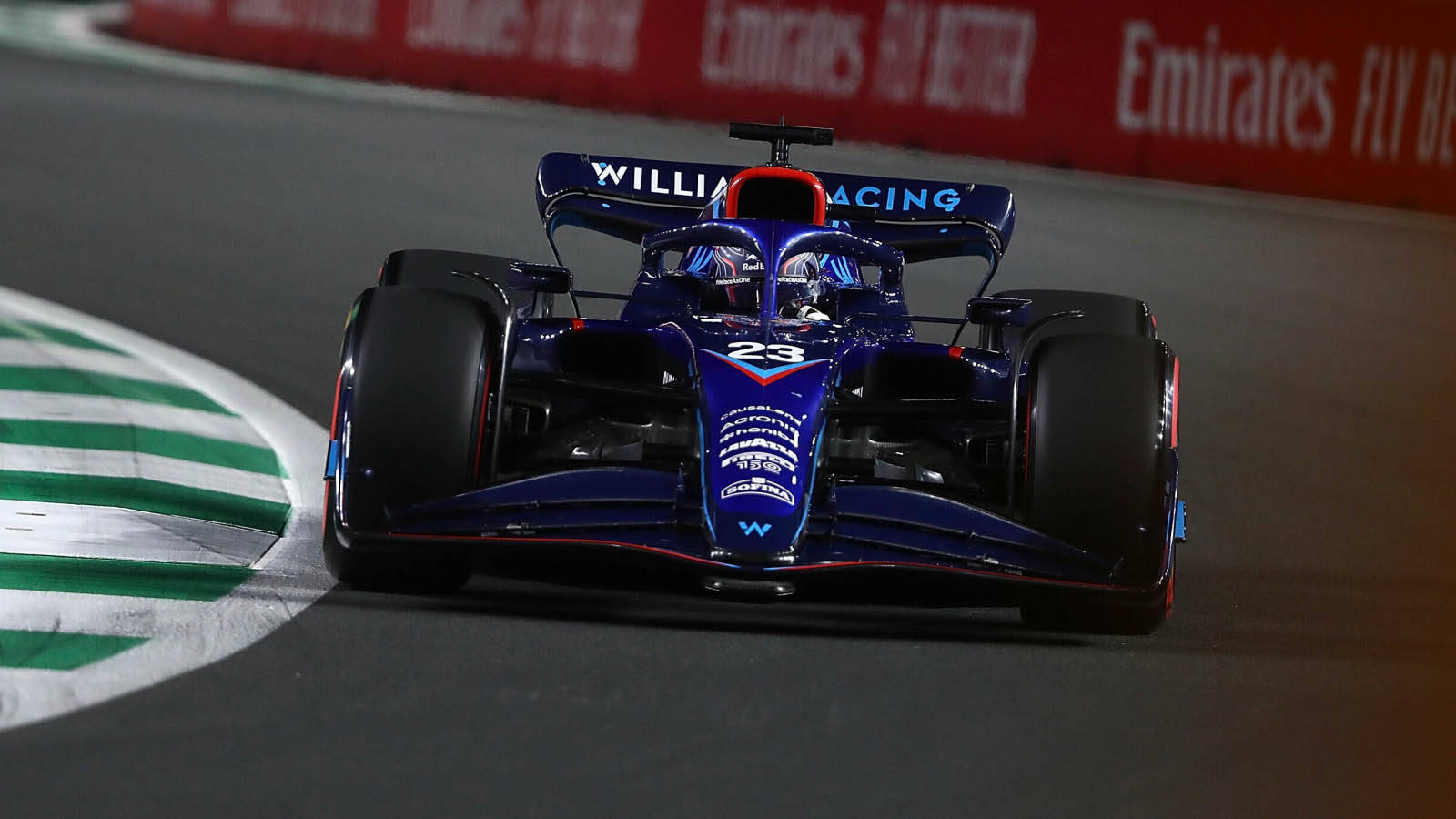藍色和紅色的 Formula 1 賽車在夜間賽道上疾馳，賽道設有綠色路緣。 — 賽車 壁紙