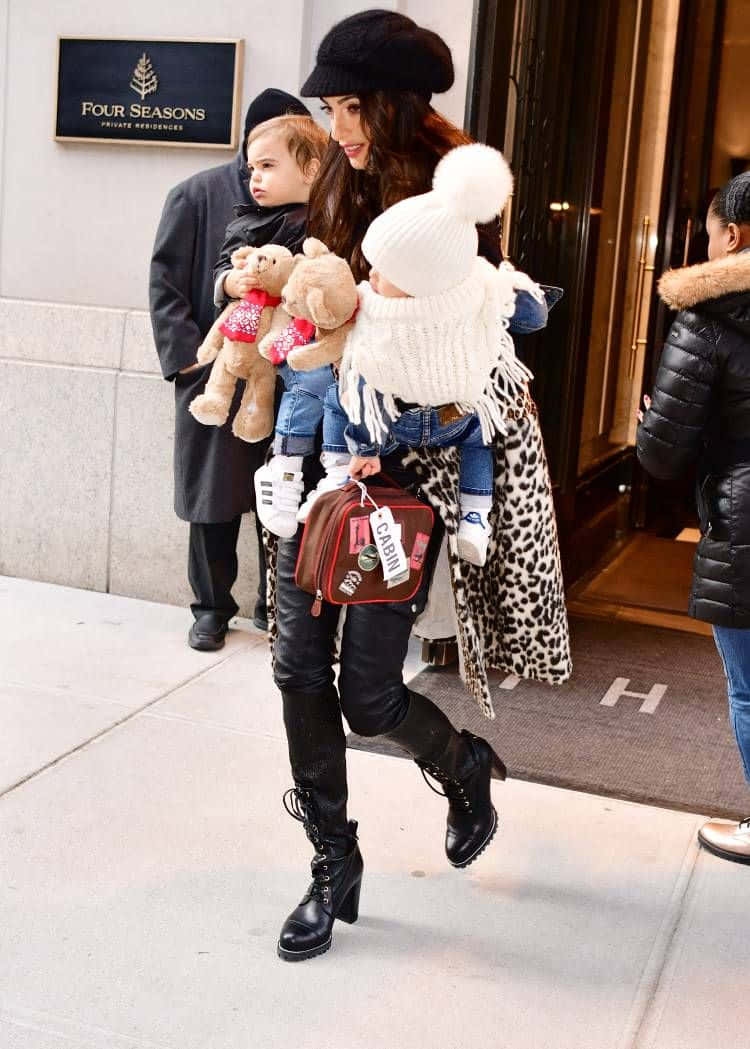 一位穿著冬季服裝的女性在豪華酒店外抱著兩個幼兒。