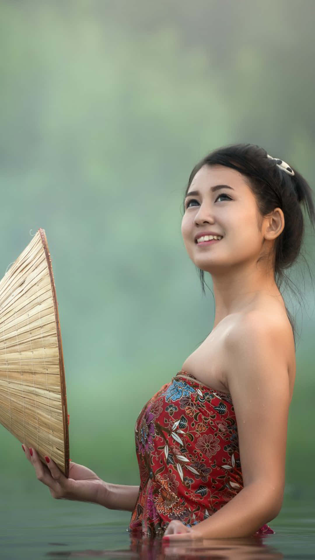 一位身穿紅色連衣裙的女子在迷霧的水中手持竹扇。