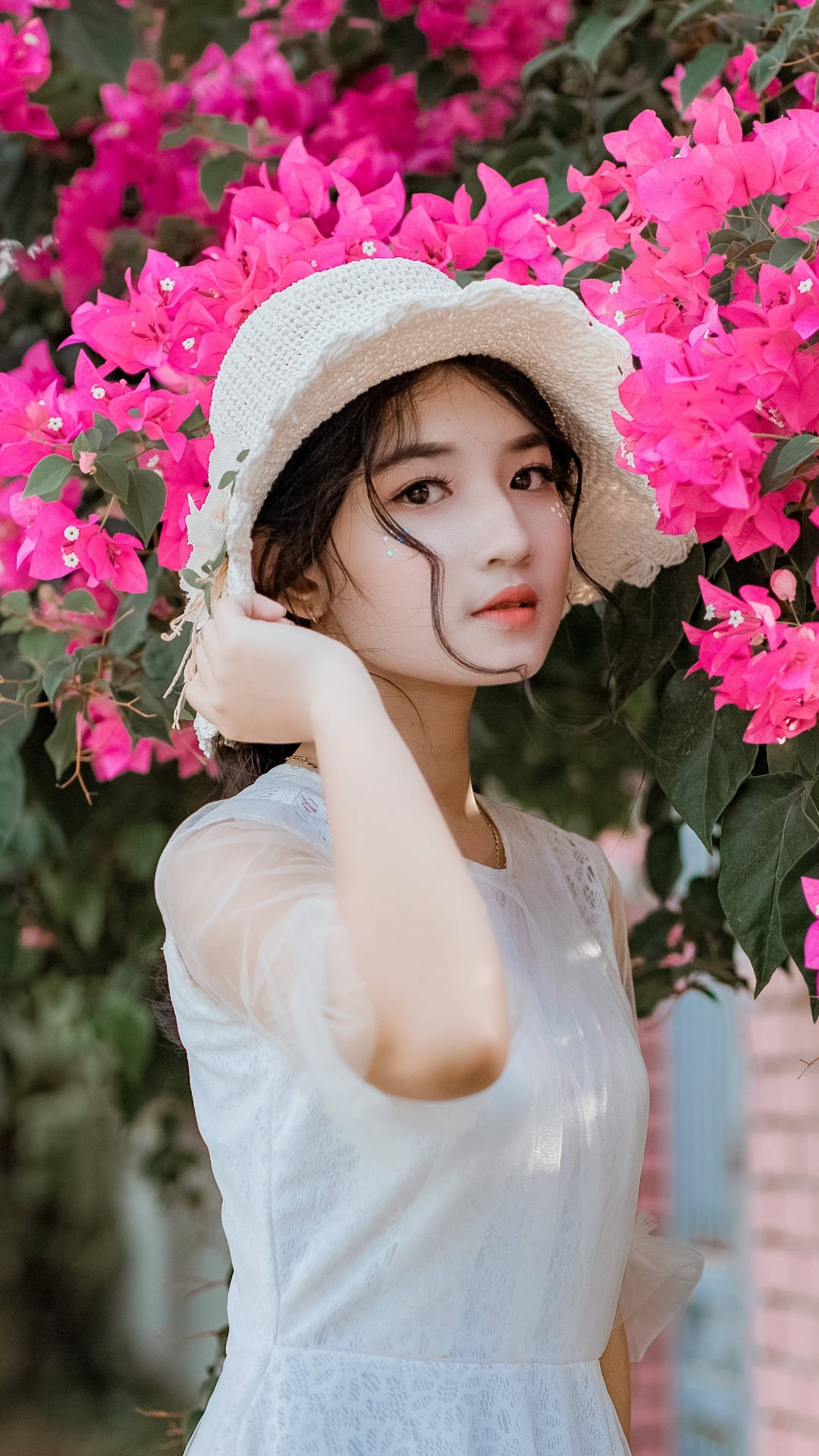 年輕女子身穿白色連衣裙和草帽，被粉紅色三角梅包圍。
