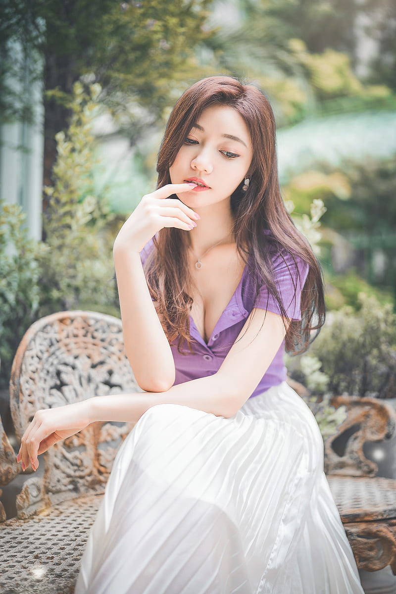 身穿紫色上衣和白色裙子的女士坐在華麗的花園長椅上