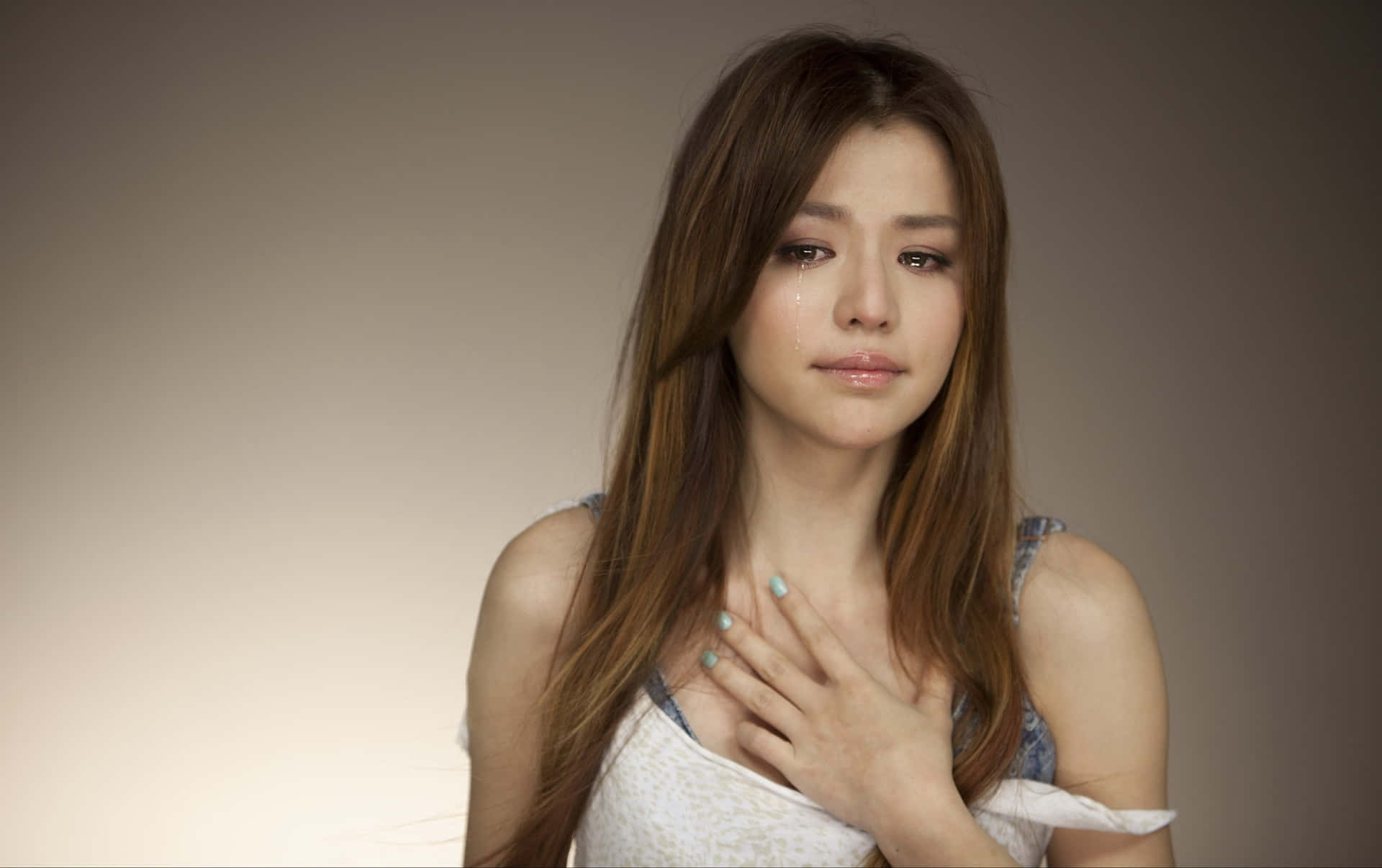 一位臉上帶著淚水的女性在攝影棚中輕柔地觸碰胸口。