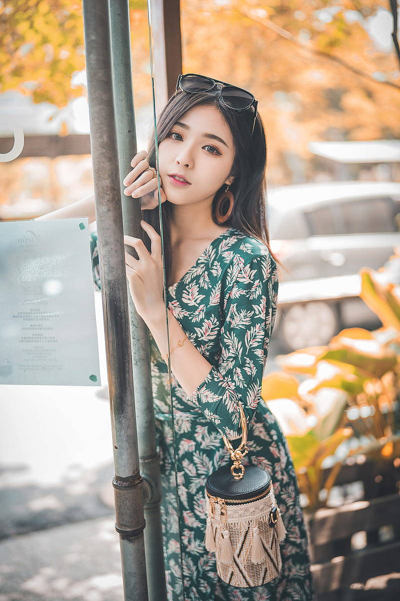 身穿花卉連衣裙的年輕女性靠著柱子，身後有秋葉。