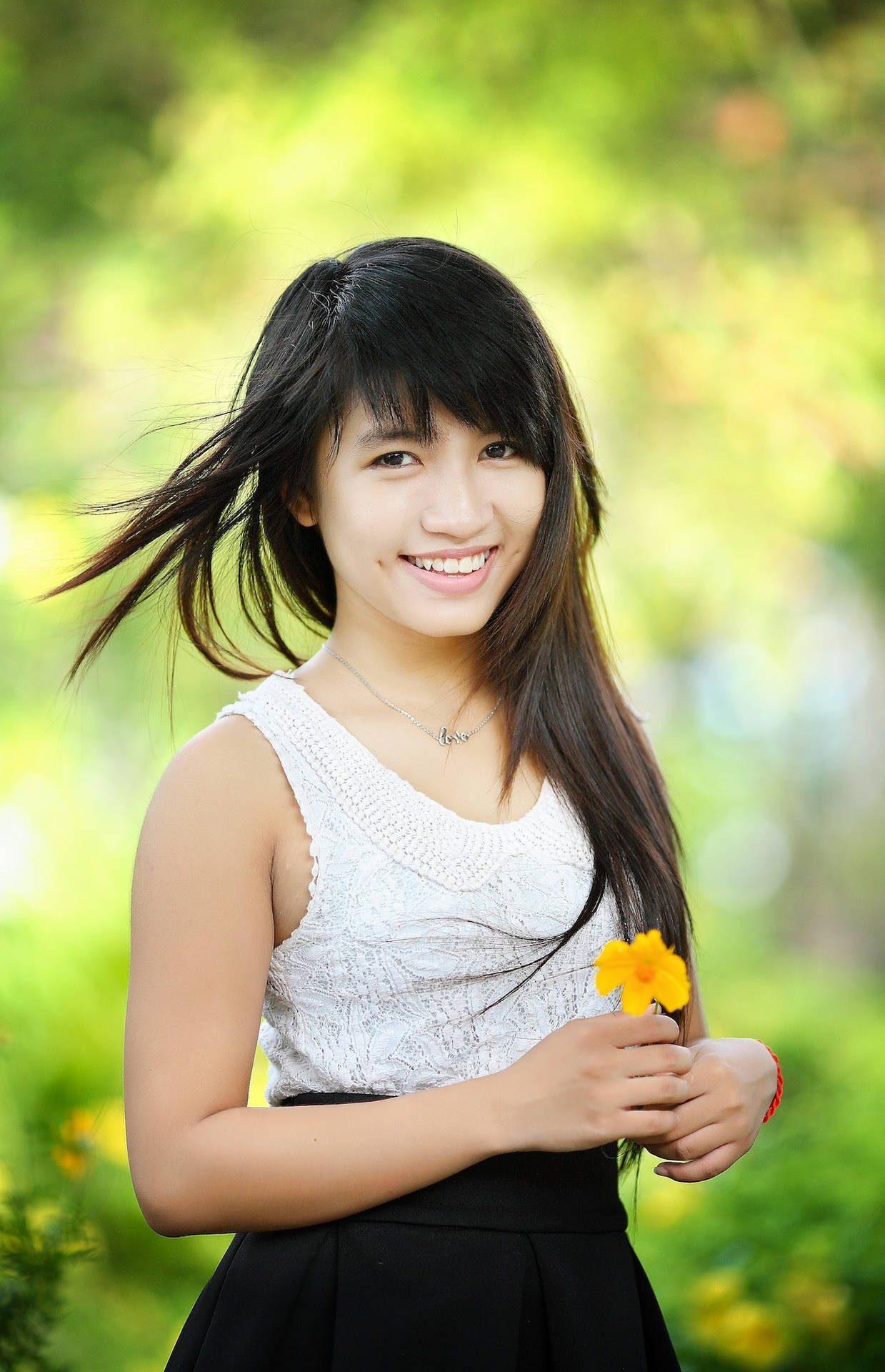 年輕女性在陽光花園中微笑著手持一朵黃色花朵。