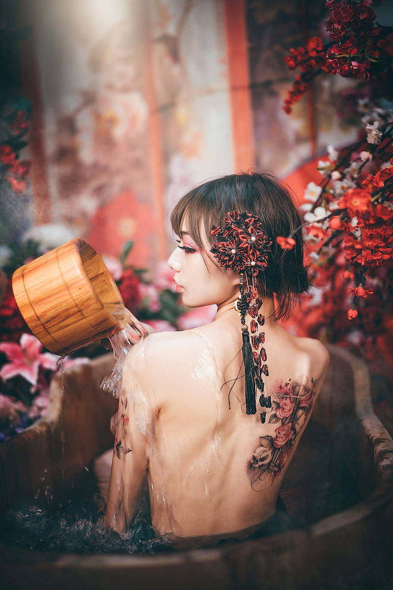 戴著花卉頭飾的女士將水倒入被紅花環繞的木浴盆中。