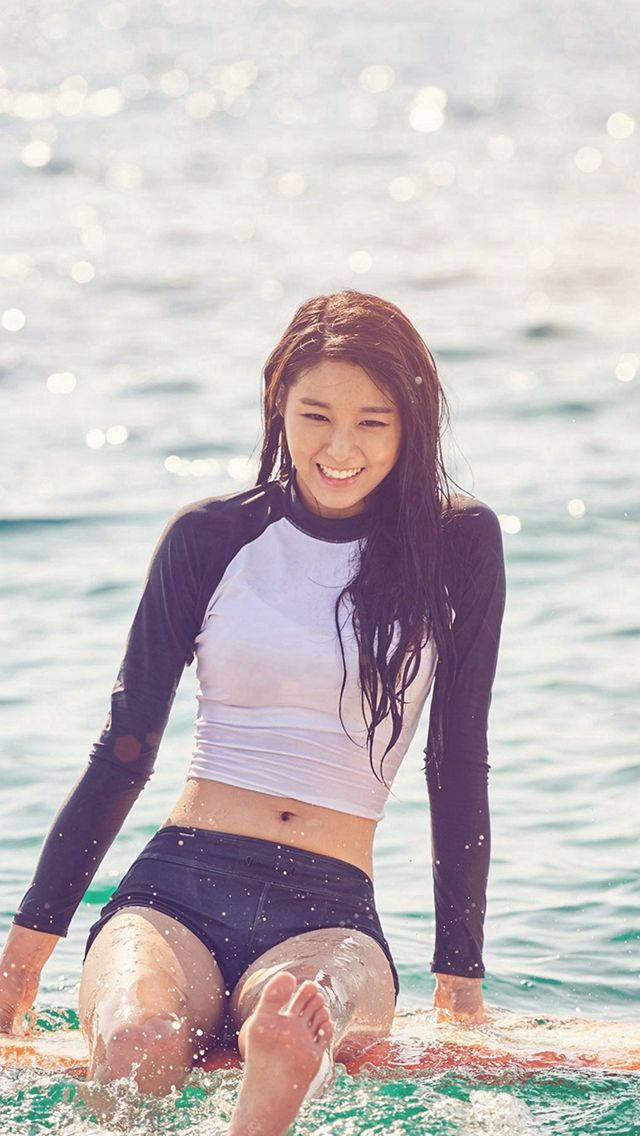 微笑女子穿防曬衣坐在海中衝浪板上
