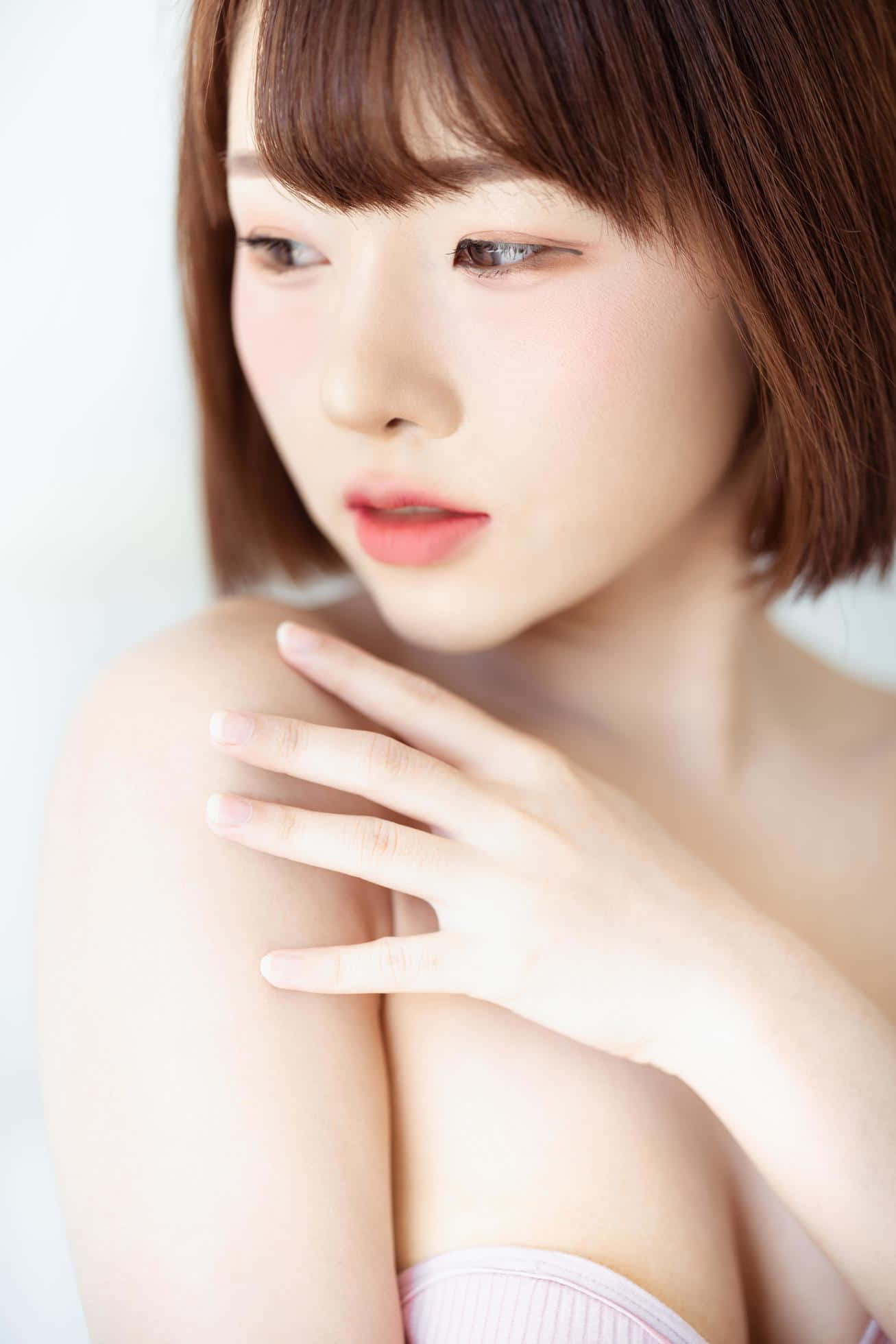 亞洲模特兒 壁紙 — 一位短棕髮的年輕女性，在柔和的白色背景上輕輕觸碰她的肩膀。