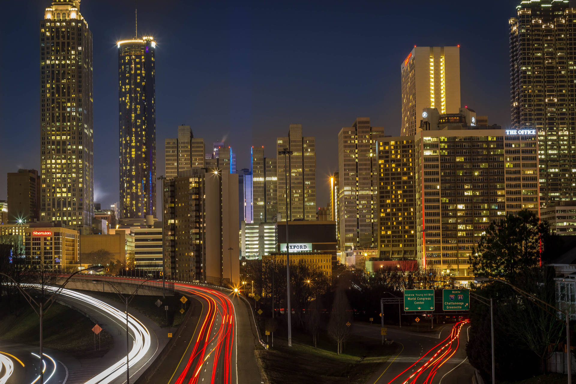亞特蘭大天際線高速公路 壁紙 — 充滿活力的夜景城市景觀，有發光的摩天大樓和彎曲高速公路上車流留下的光跡。