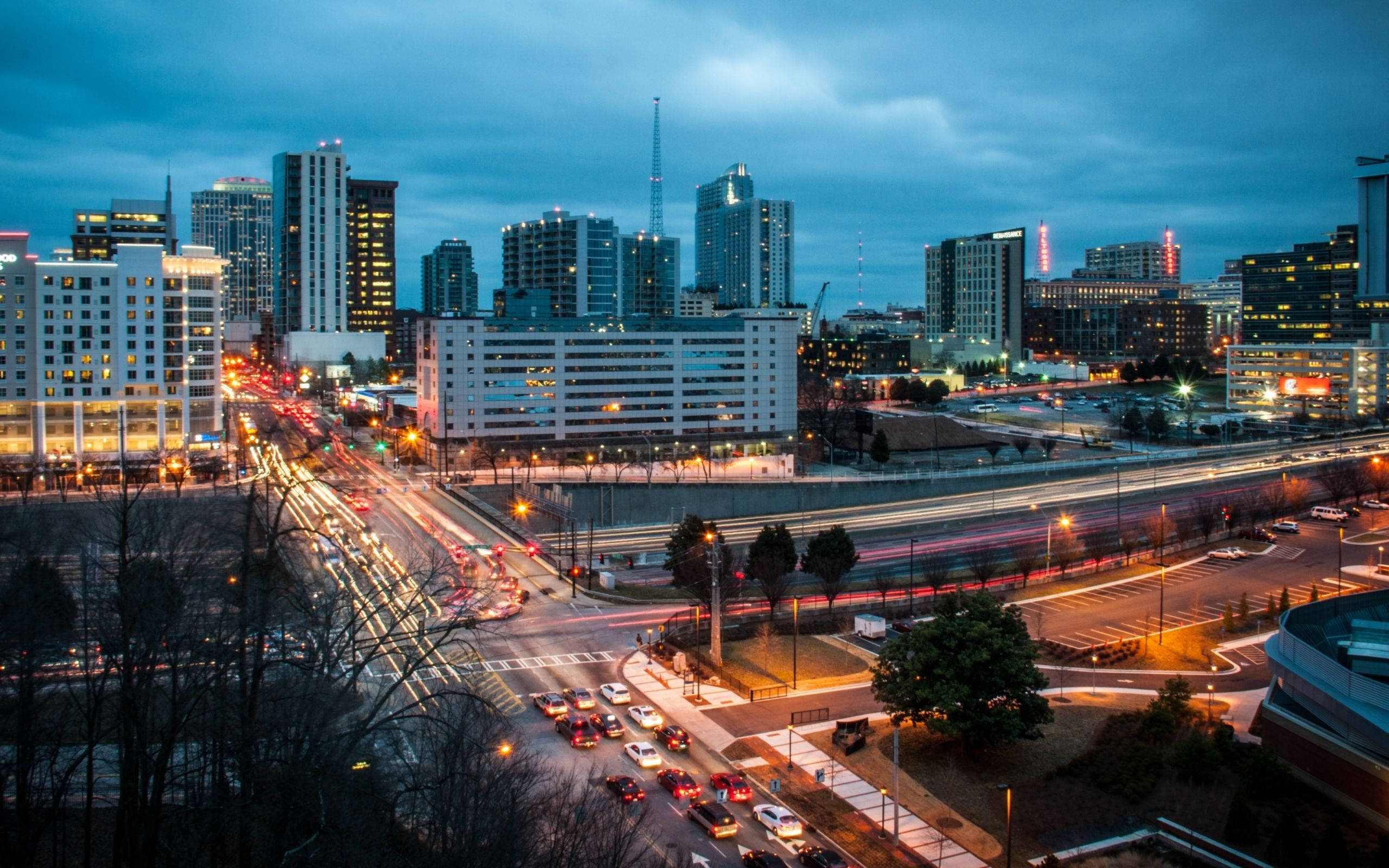亞特蘭大市中心夜景燈光 壁紙 — 黃昏時分充滿活力的城市景觀，在憂鬱的藍天下，汽車燈光劃過，摩天大樓燈火通明。