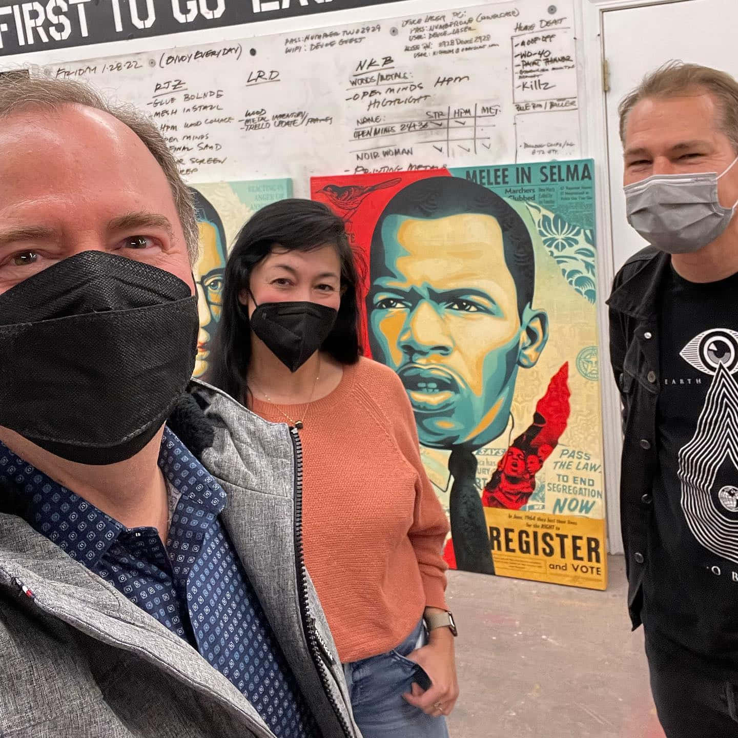 三名戴著口罩的個體站在帶有手寫筆記的馬丁·路德·金抗議壁畫前。