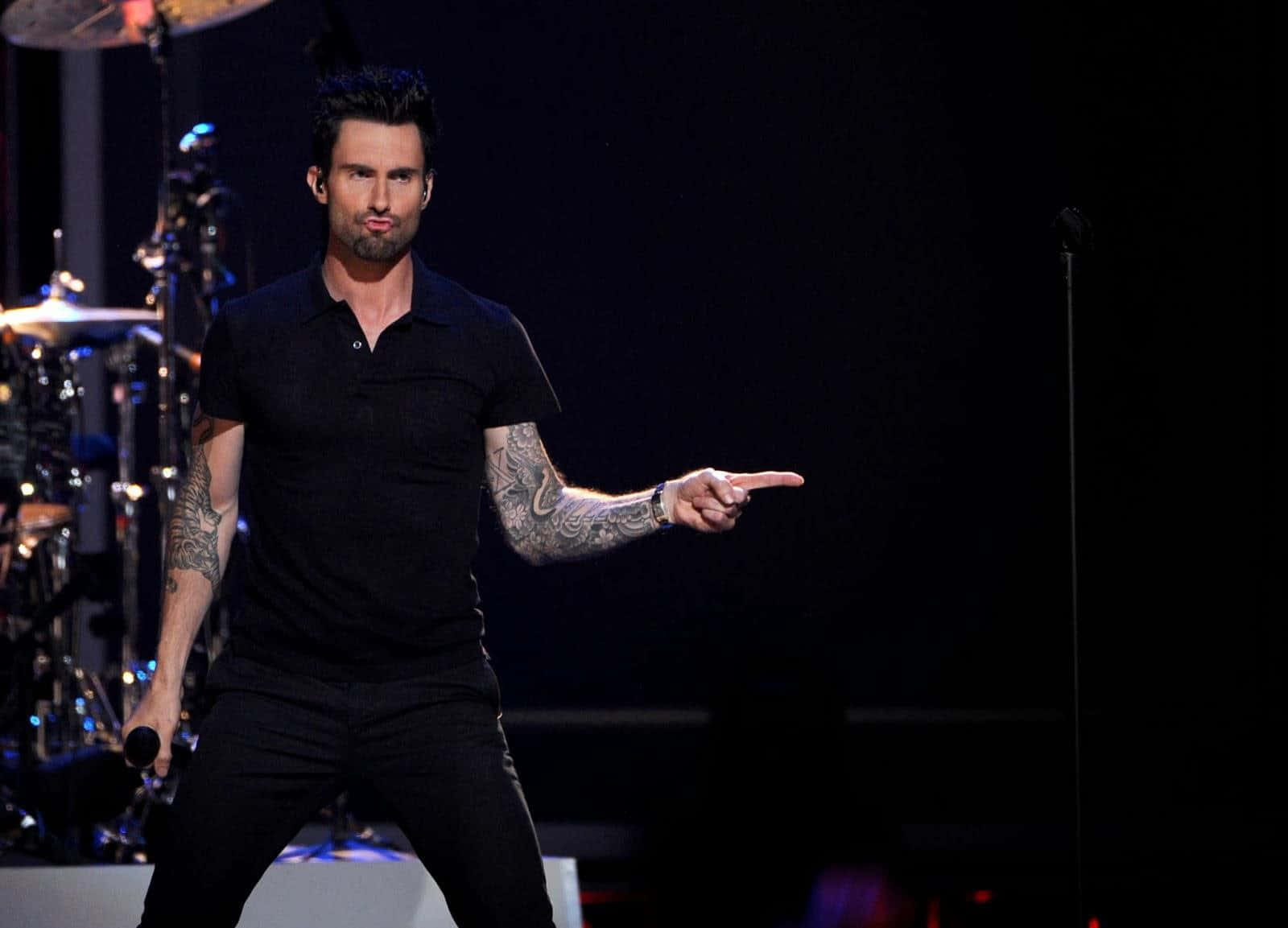 亞當·萊文於MTV Unplugged演出 壁紙 — Adam Levine 身穿黑色服裝在舞台上表演，向前指著，舞台燈光下可見紋身。
