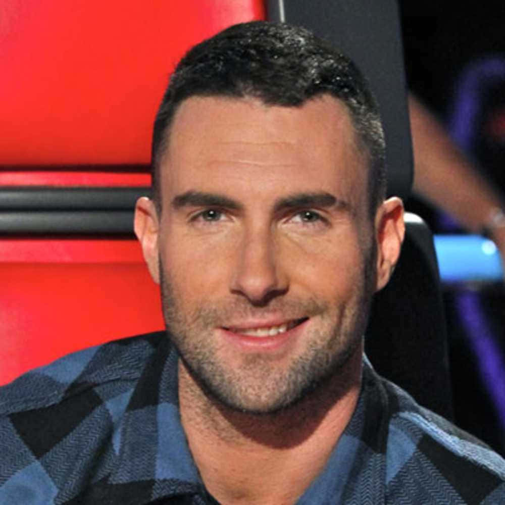 亞當·萊文是流行樂隊Maroon 5的成員 壁紙 — Adam Levine 溫暖地微笑，坐在紅色椅子上，穿著藍黑格仔襯衫。