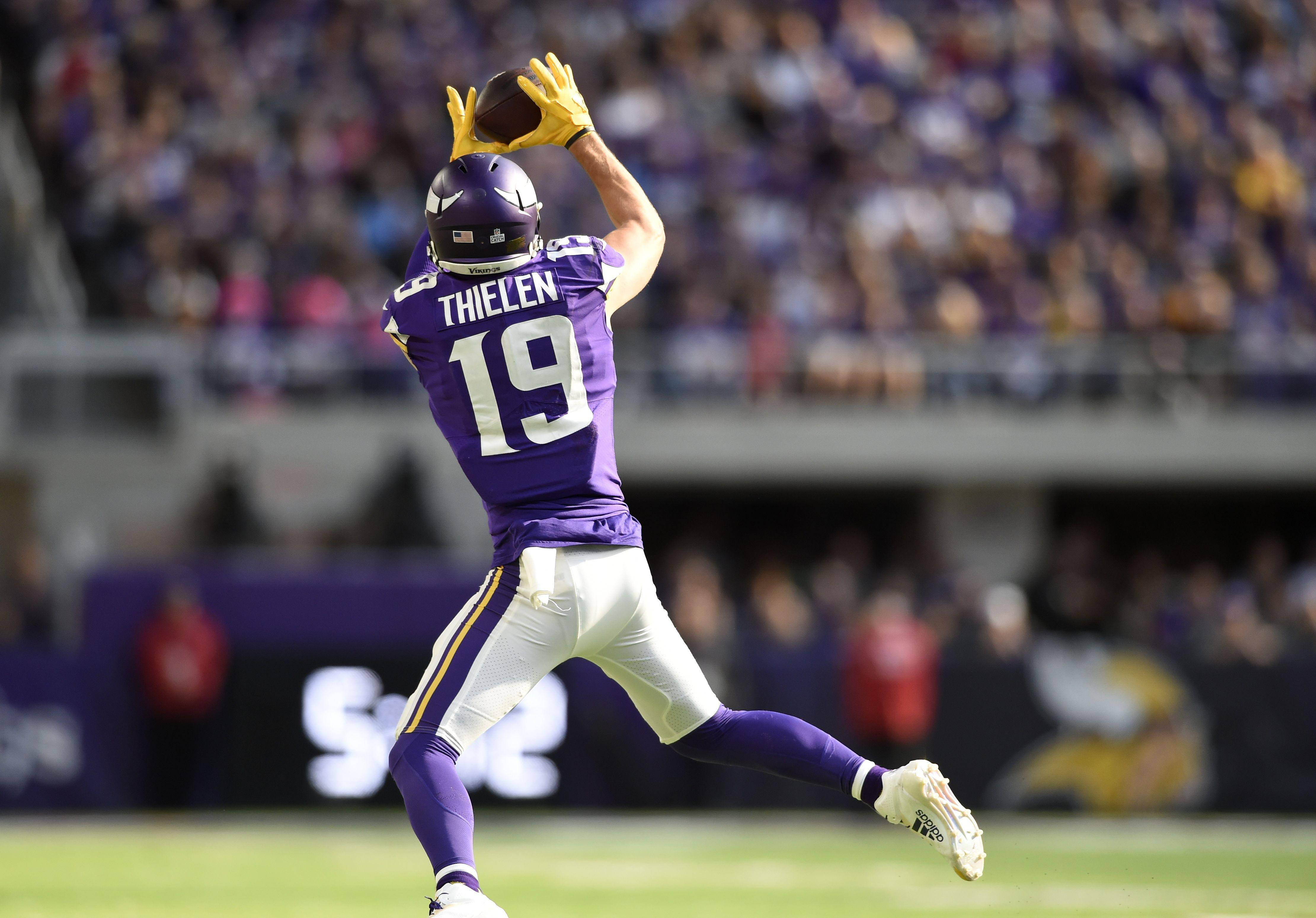 亞當·西倫的NFL職業生涯 壁紙 — 一名身穿紫色19號球衣的美式足球員戴著黃色手套跳起接球，背景是模糊的體育場人群。