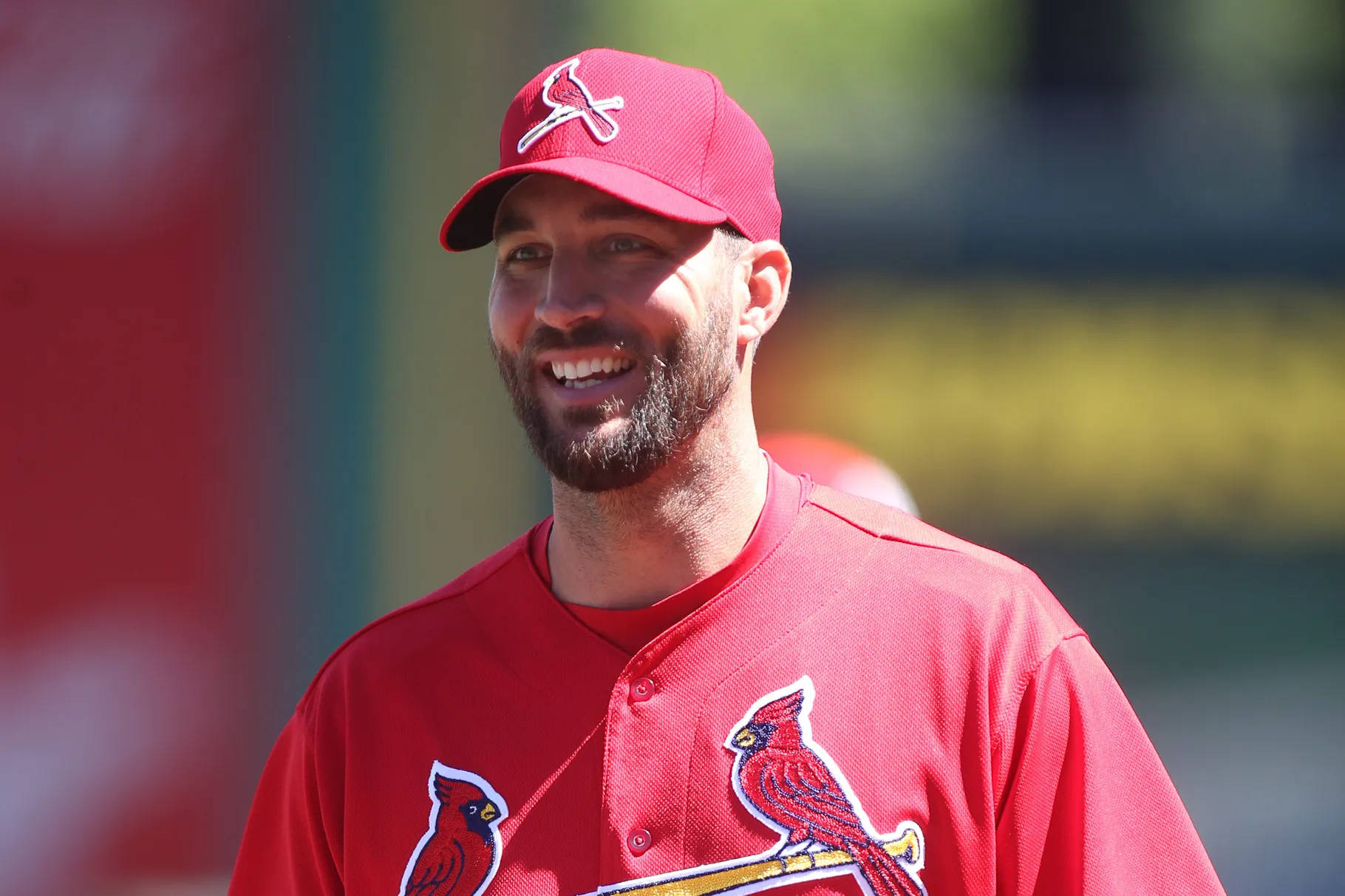 身穿紅色 Cardinals 球衣的棒球運動員在戶外微笑。