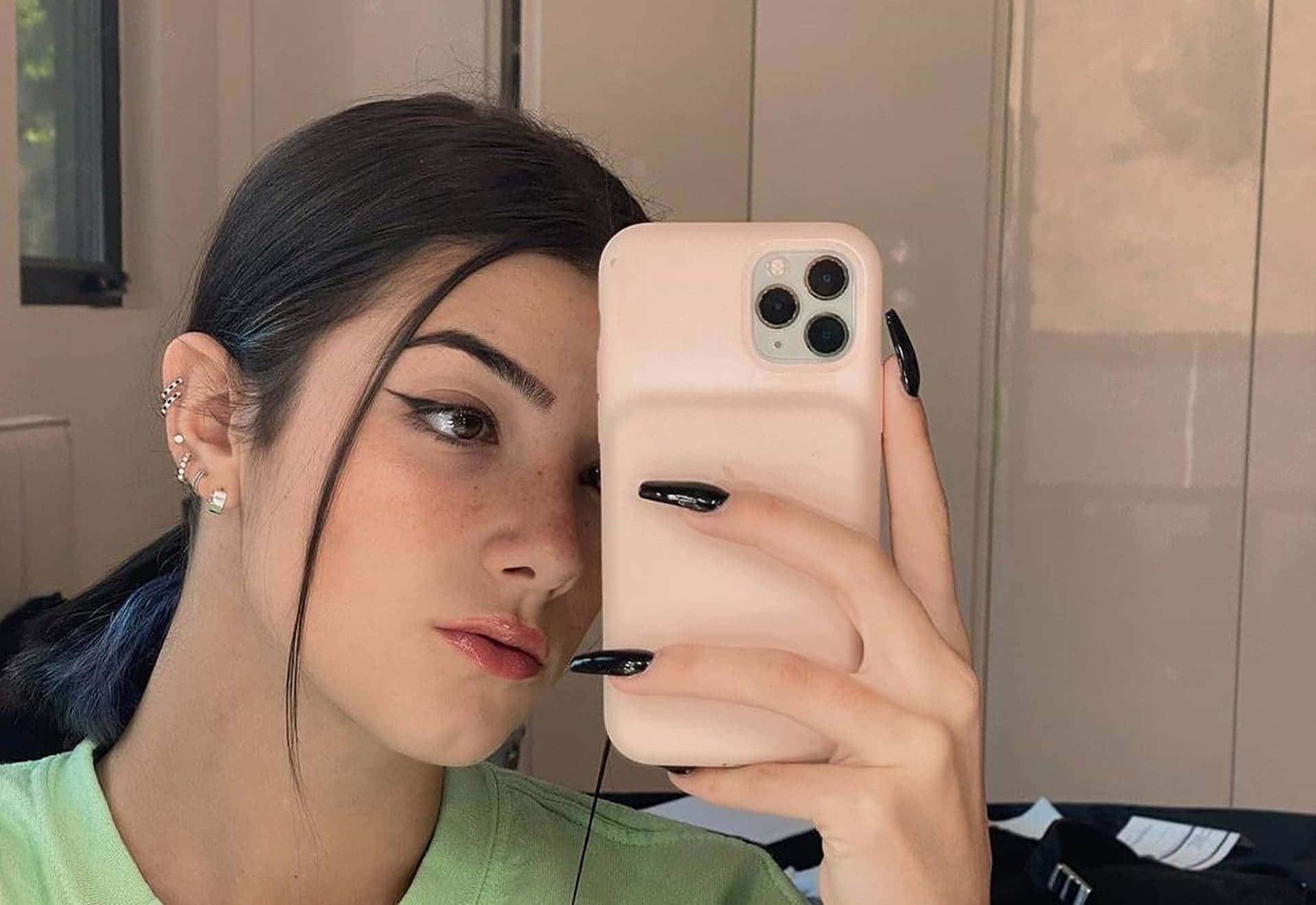 年輕女子在室內用手機和黑色指甲油在鏡子前自拍。