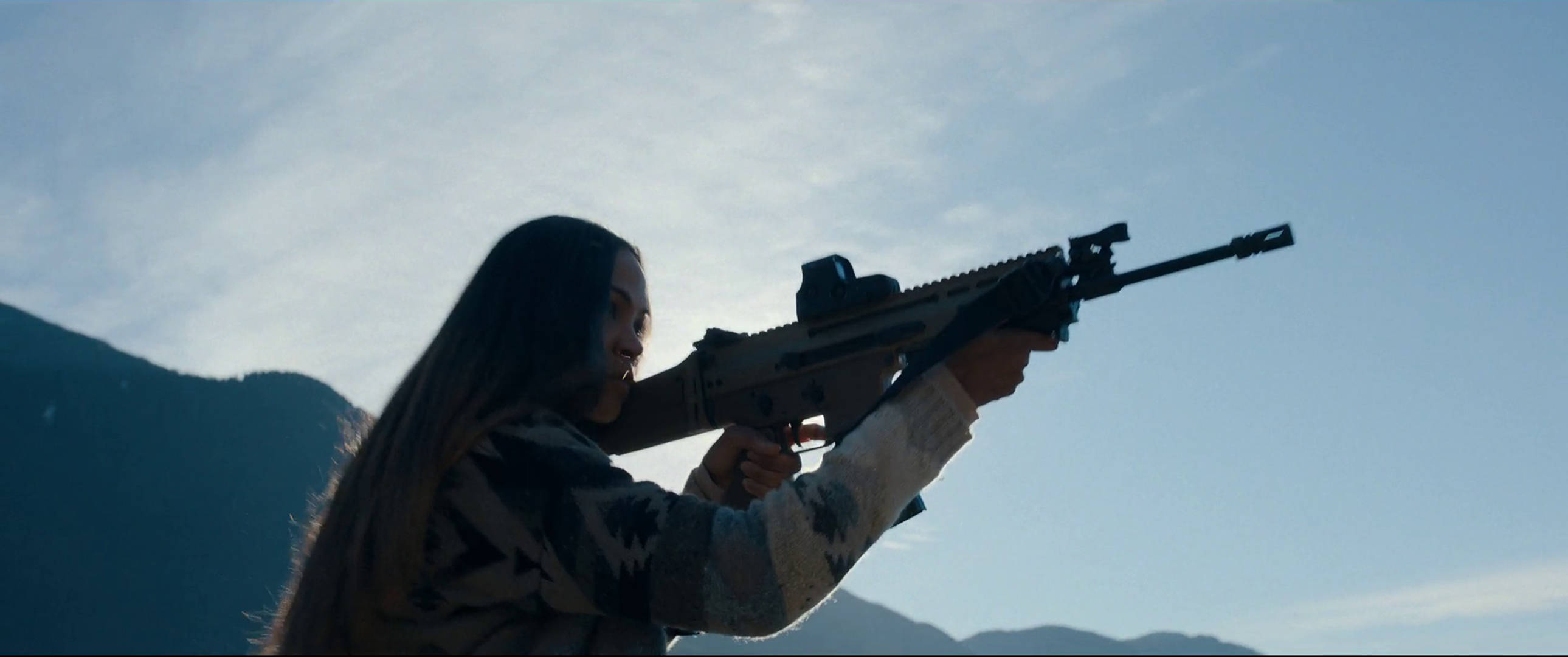 《亞當計劃》SCAR步槍 壁紙 — 一名身穿迷彩服嘅女人喺山脈同晴朗藍天背景下瞄準步槍。