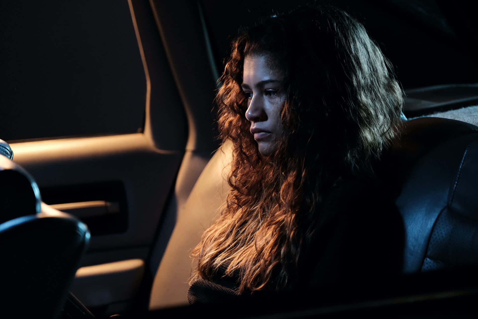 捲髮女人夜晚坐在車裡，神情沉思。