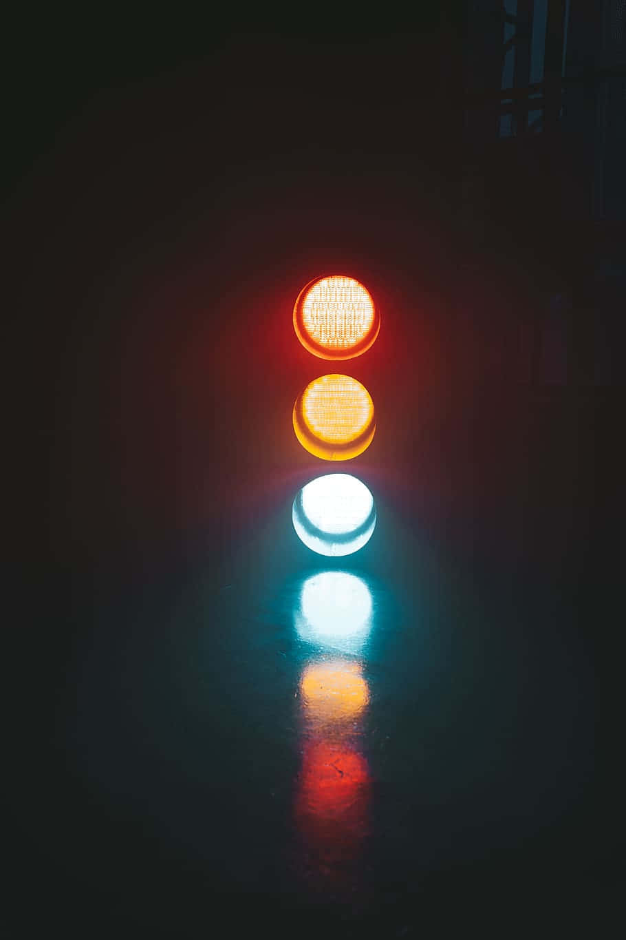 交通燈在夜間潮濕路面上發出紅色、黃色和綠色的光芒。
