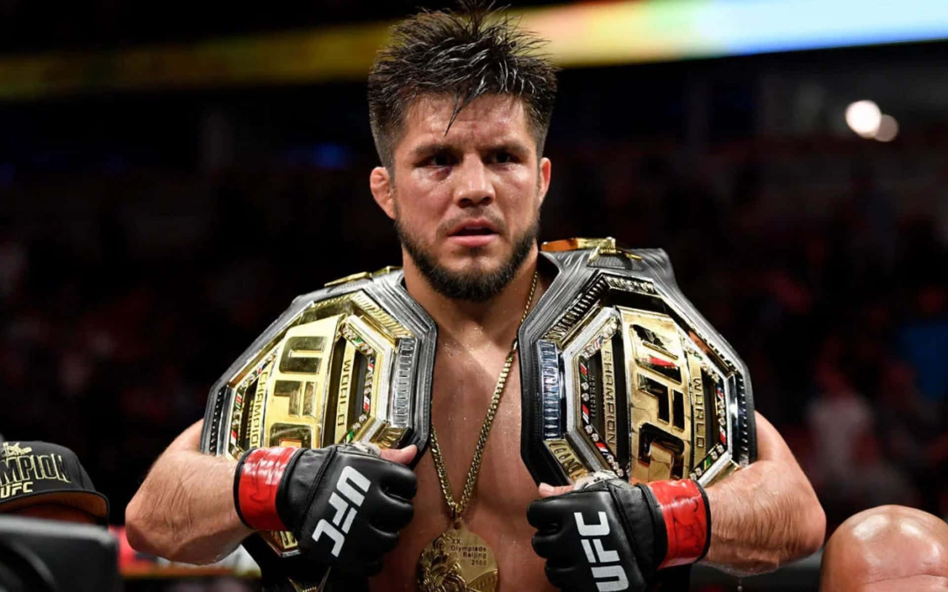 亨利·塞胡多TKO擊敗馬龍·莫拉埃斯UFC 238 壁紙 — 一位勝利的UFC拳手，臉上閃爍著汗水，在明亮的競技場中將兩條冠軍腰帶扛在肩上。
