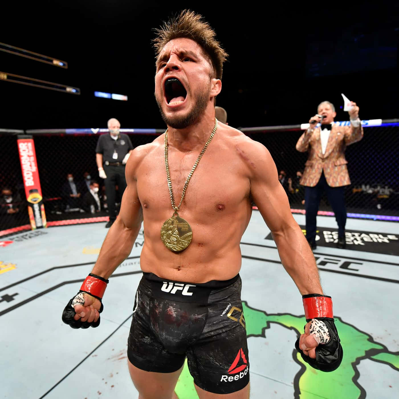 亨利·塞胡多在UFC 238擊倒馬龍·莫拉埃斯 壁紙 — 一位勝利的UFC拳手在八角籠中戴著金牌和沾滿血跡的短褲，發出勝利的怒吼。