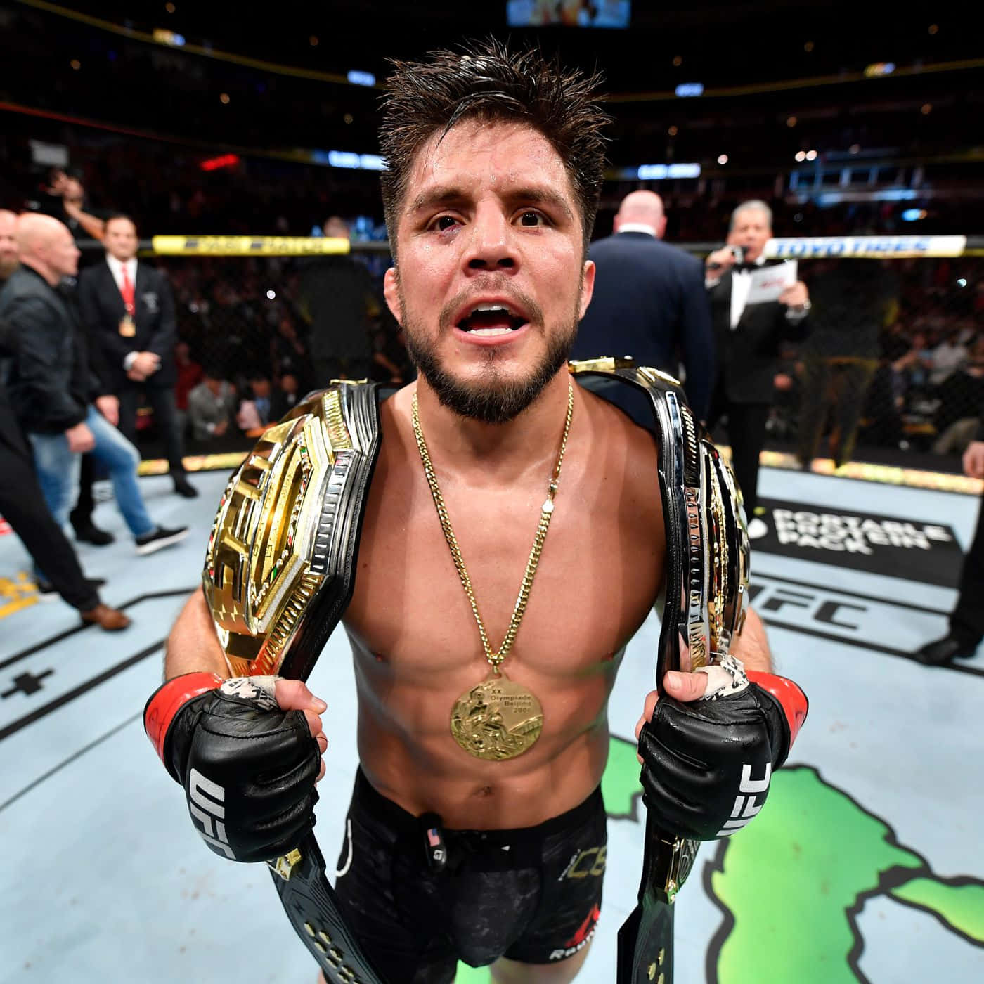 亨利·塞胡多在UFC 238擊敗馬龍·莫拉埃斯 壁紙 — 一位勝利的UFC拳手在明亮的場館燈光下，於八角籠中自豪地展示他的冠軍腰帶。