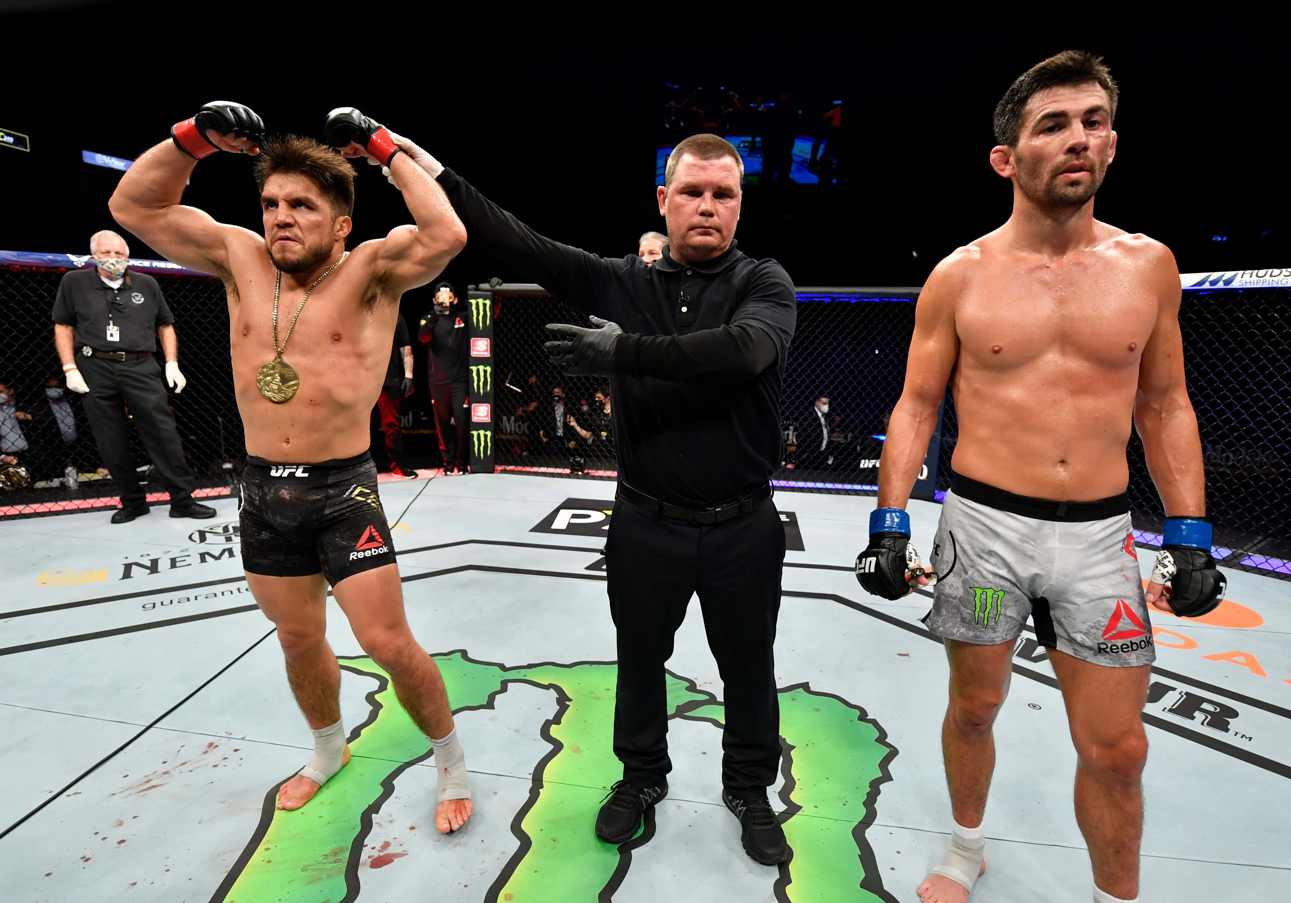 亨利·塞胡多對決多米尼克·克魯茲 UFC 249 壁紙 — 一位勝利的UFC拳手高舉雙臂，裁判舉起他的手以示勝利，而他的對手則沮喪地站在八角籠中。