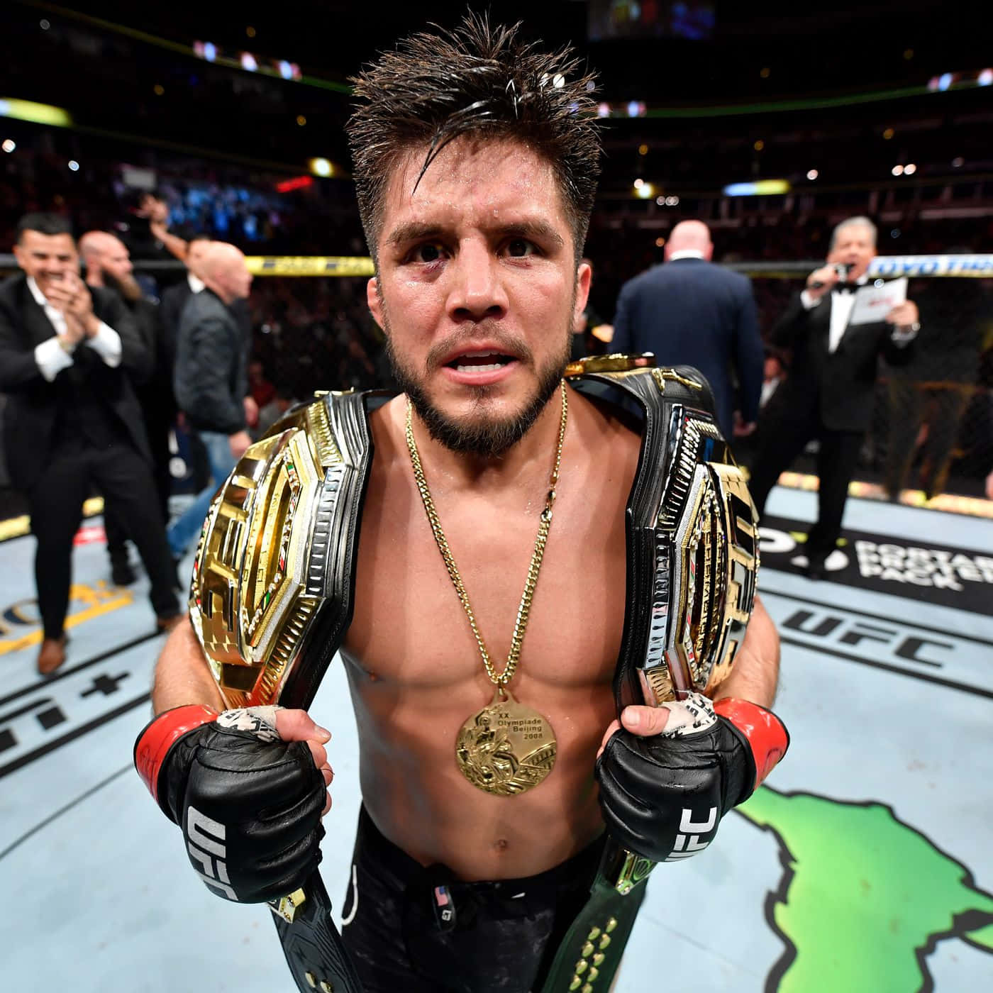 亨利·塞胡多慶祝2019年奪得鈴鐺級冠軍 壁紙 — 一位勝利的UFC拳手站在八角籠中，手持兩條冠軍腰帶，脖子上掛著金牌。