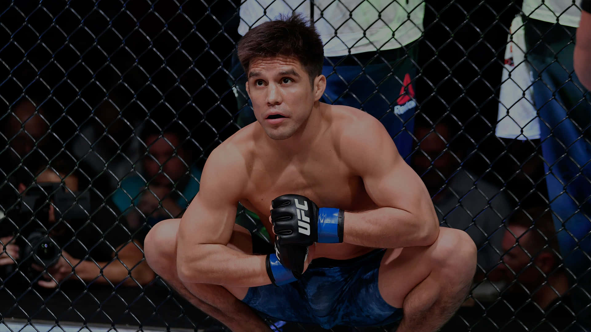 亨利·塞胡多於 UFC 227 賽事 壁紙 — 一名肌肉發達的戰士蹲在UFC八角籠內，穿著藍色短褲和黑色手套，神情專注。