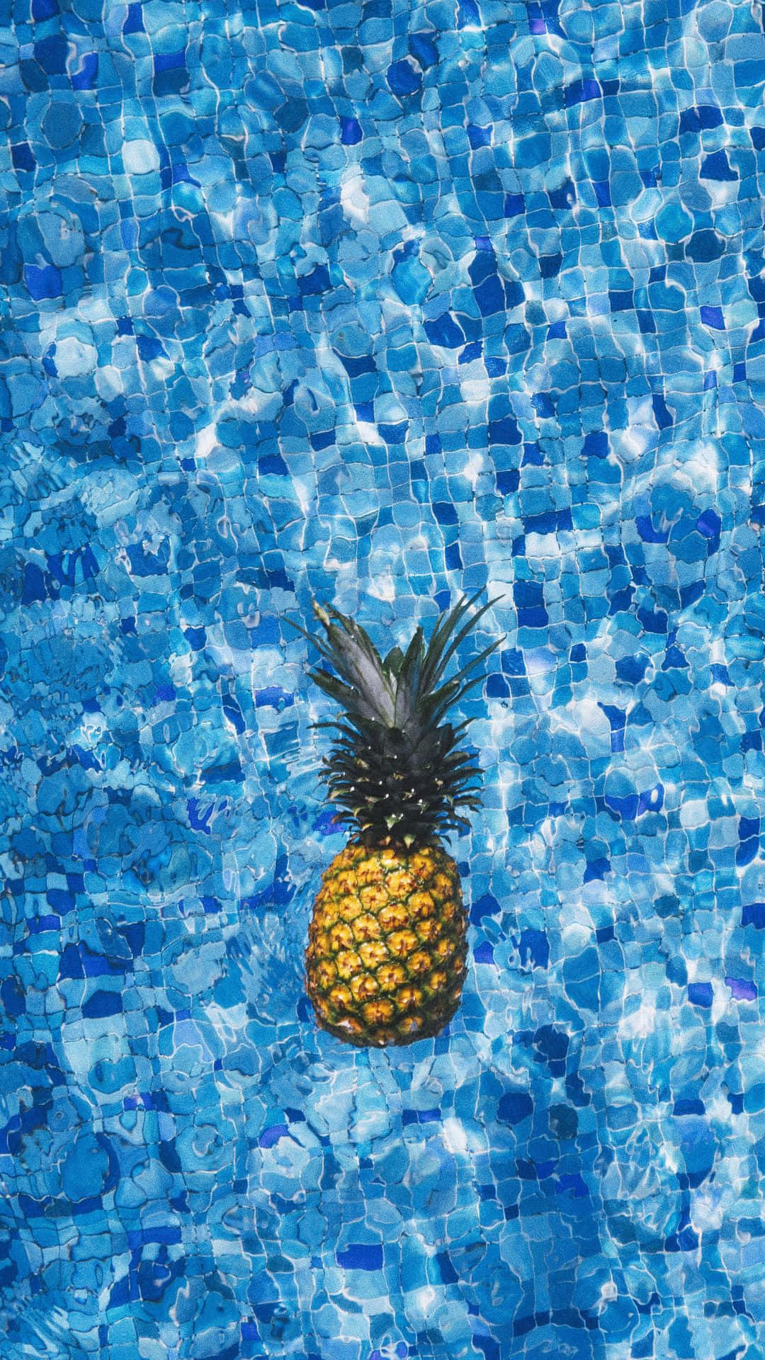 享受 Android 夏日 壁紙 — 一個成熟的菠蘿在陽光普照的藍色馬賽克瓷磚泳池中靜靜漂浮。