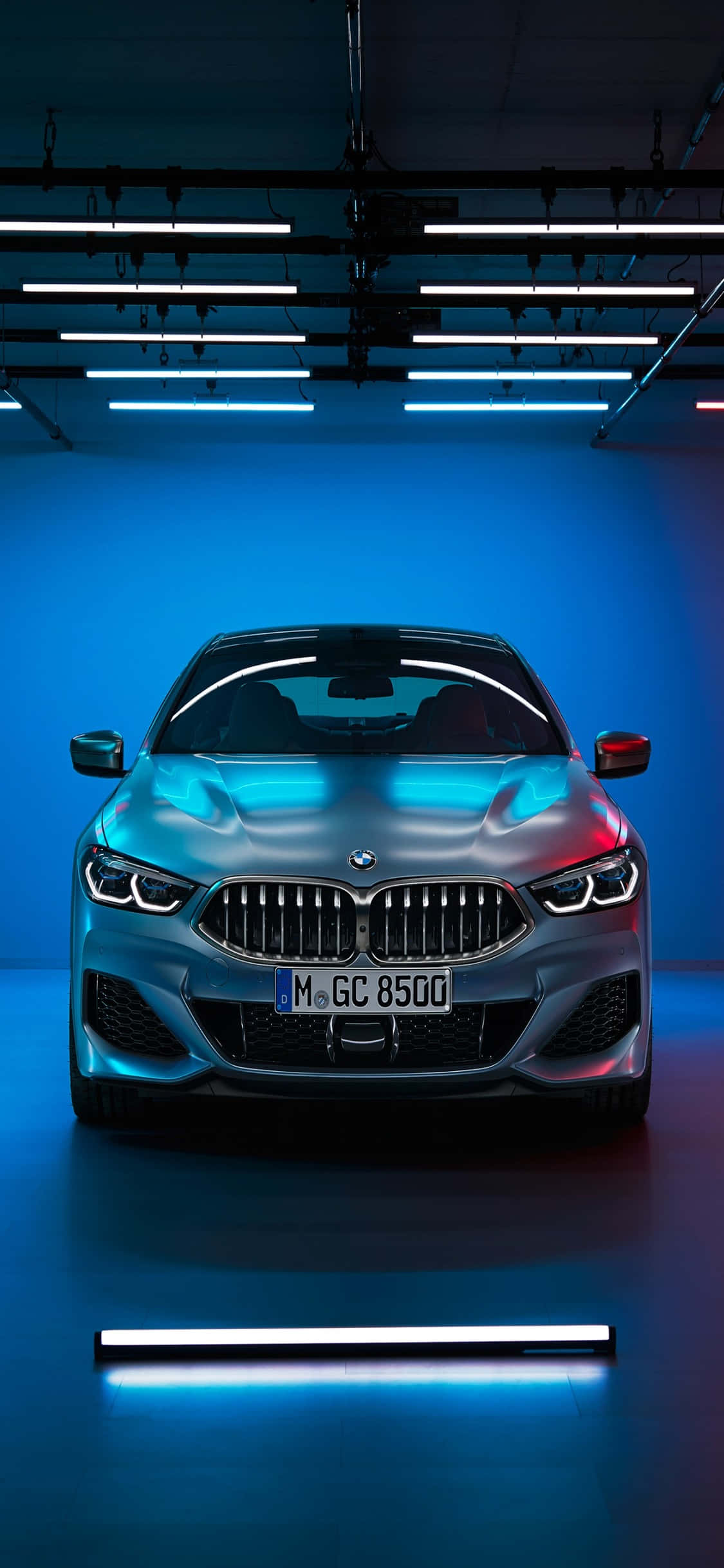 享受 iPhone X 的奢華，感受 BMW 的強勁動力 壁紙 — 一輛時尚的銀色BMW跑車在簡約車庫環境中，在酷炫的藍色霓虹燈下閃閃發光。