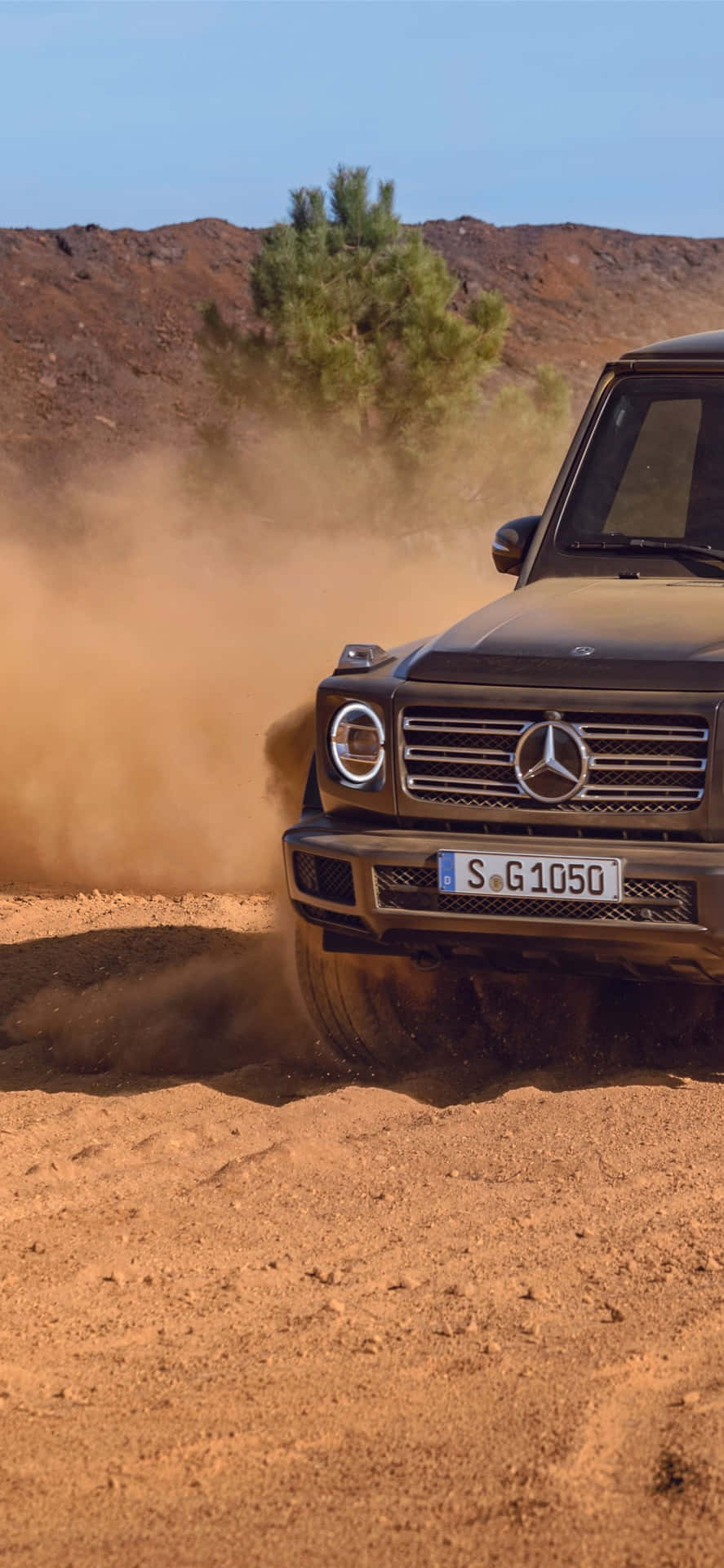 黑色 Mercedes G-Class 在沙漠地形上行駛，揚起沙塵。