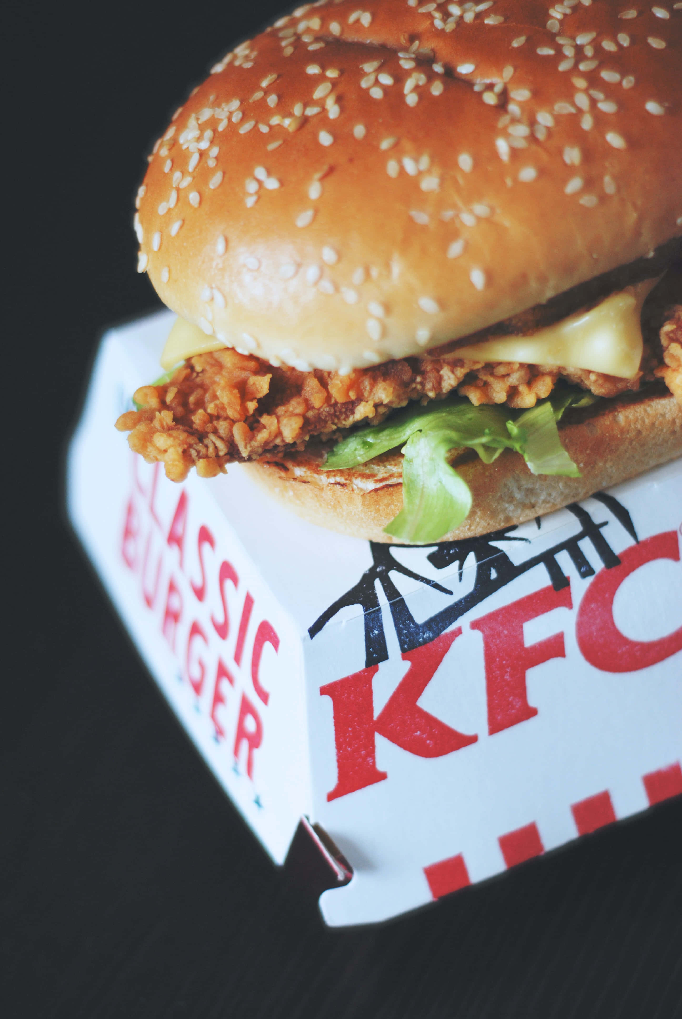 享受 KFC 炸雞的酥脆美味 壁紙 — KFC經典漢堡盒中，一個酥脆炸雞漢堡配融化芝士和生菜的特寫。