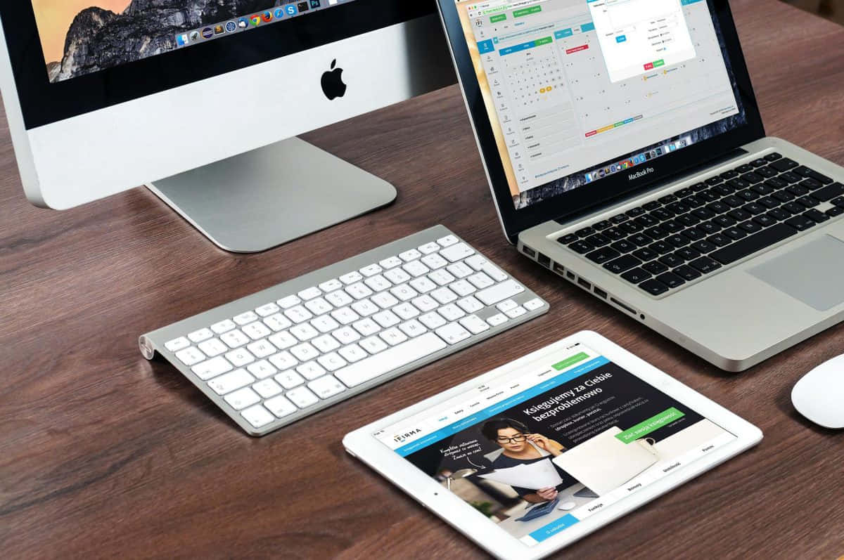 科技工作站，配備 iMac、手提電腦、平板電腦和鍵盤，置於木桌上。