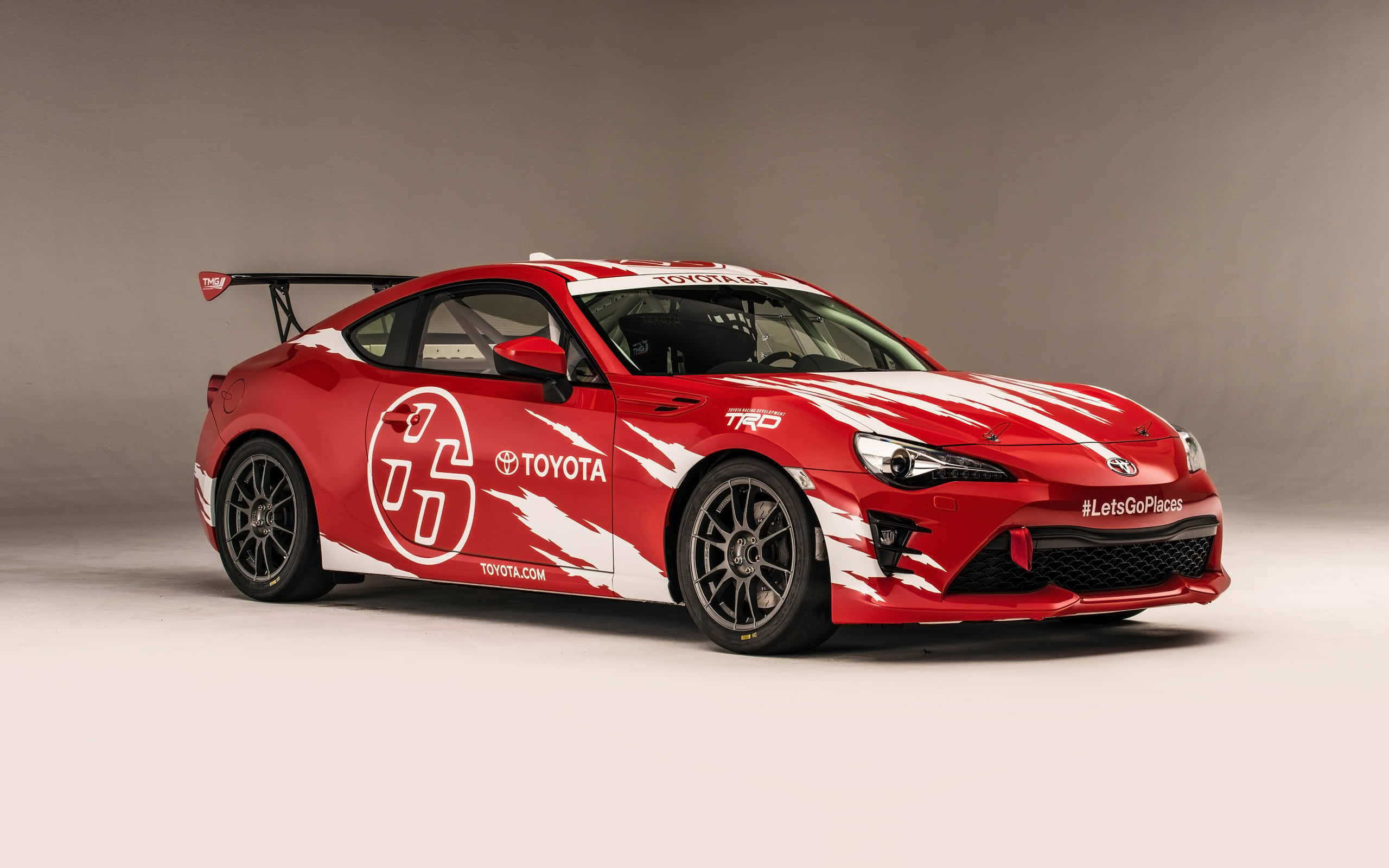 享受 Toyota 86 的順暢駕駛體驗 壁紙 — 一輛鮮紅色的豐田跑車，帶有白色賽車條紋和贊助商貼紙，在攝影棚內擺拍。
