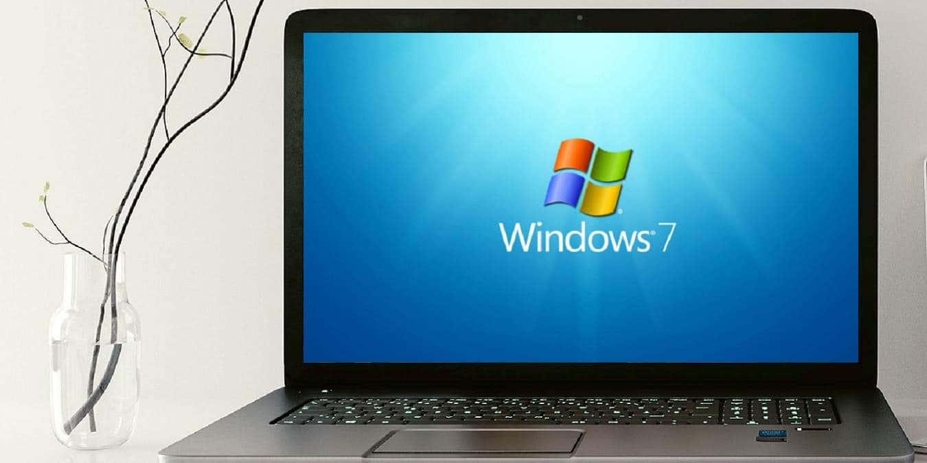 手提電腦顯示Windows 7標誌，旁邊有玻璃花瓶插著光禿樹枝。