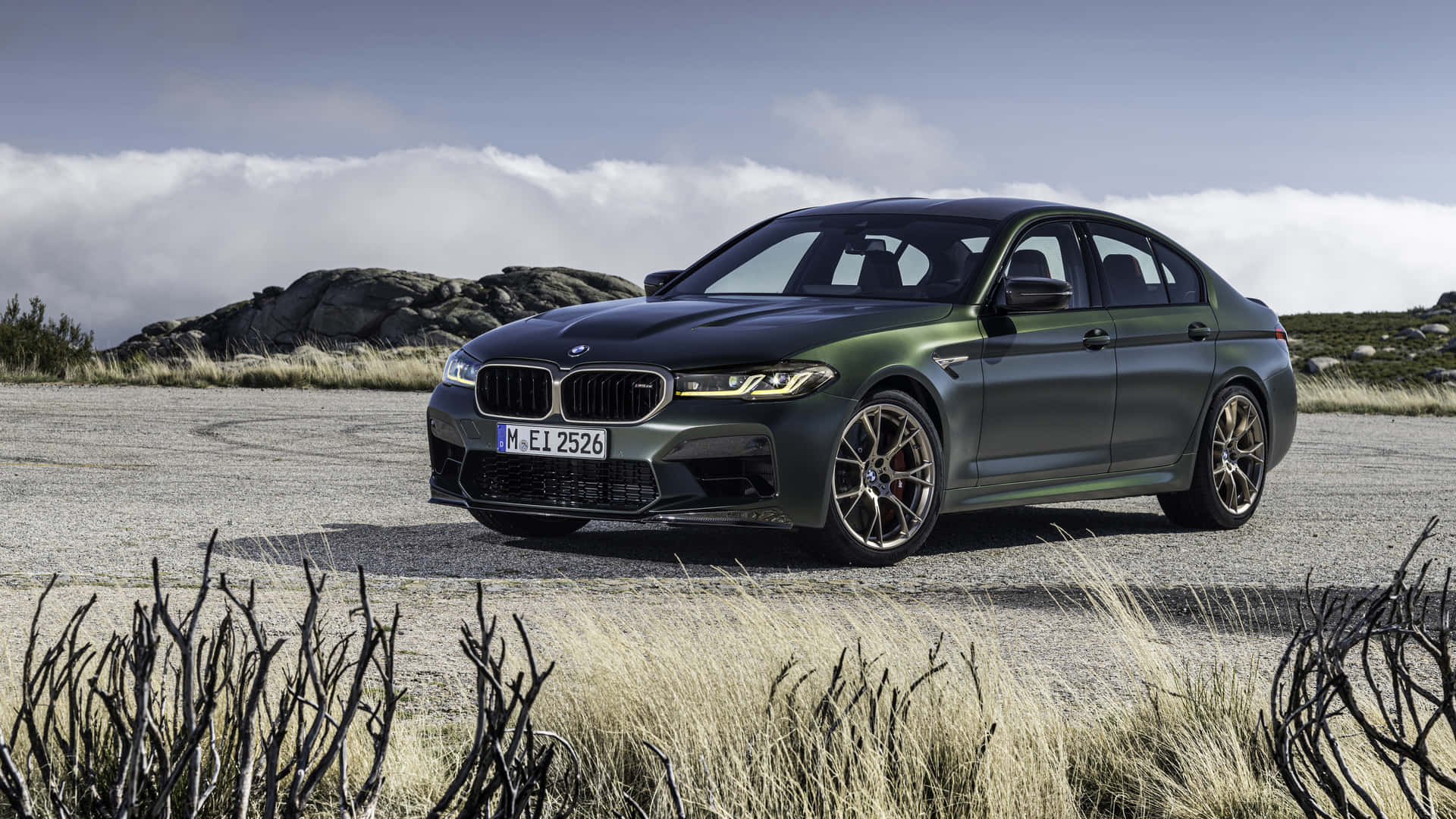 啞光綠色BMW M5停泊在碎石路上，周圍是岩石山丘和乾草。