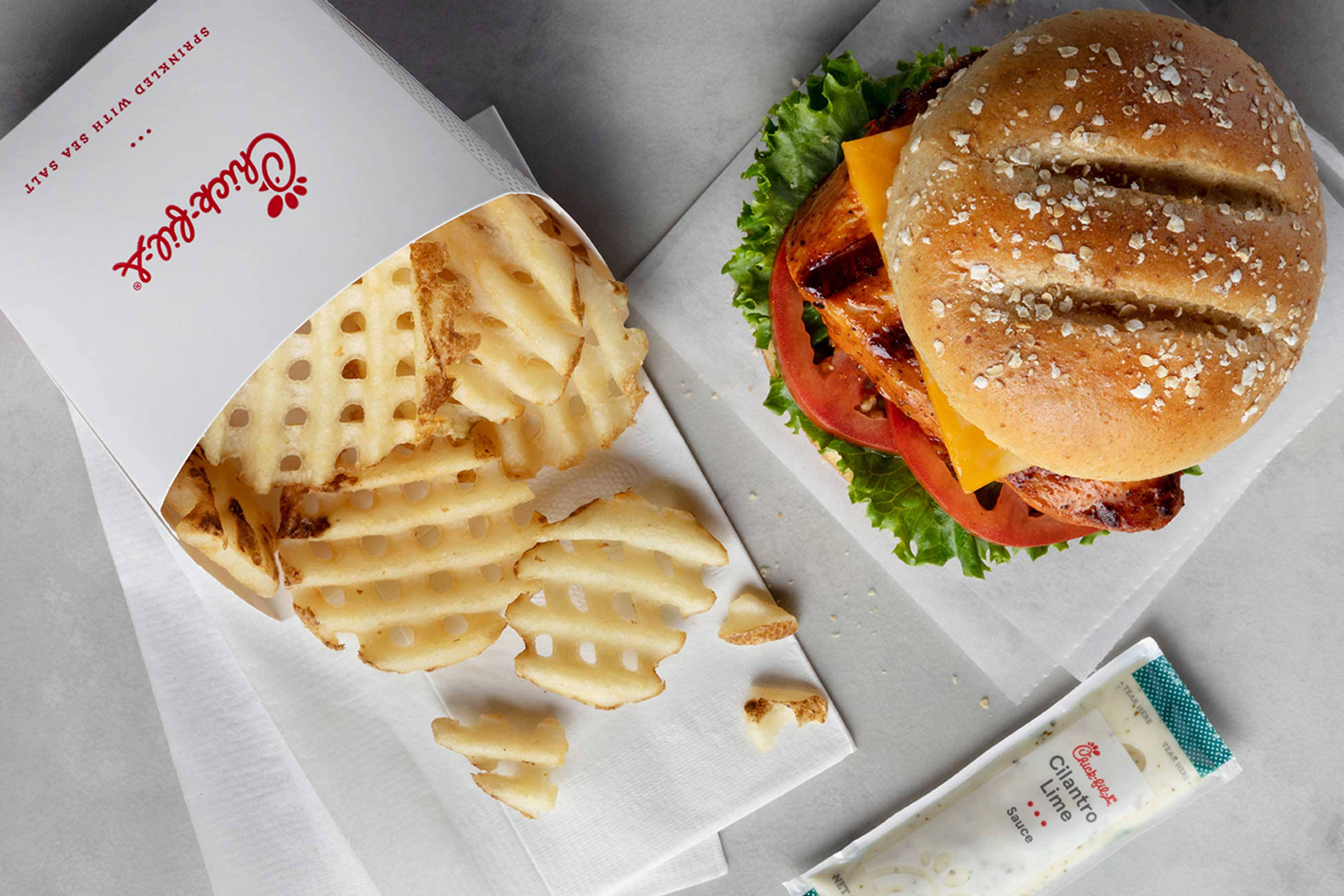 享受Chick-fil-A奢華套餐的美味 壁紙 — 一個脆皮窩夫薯條盒同一個多汁漢堡，有生菜、番茄同芝士，放喺牛油紙上嘅特寫。