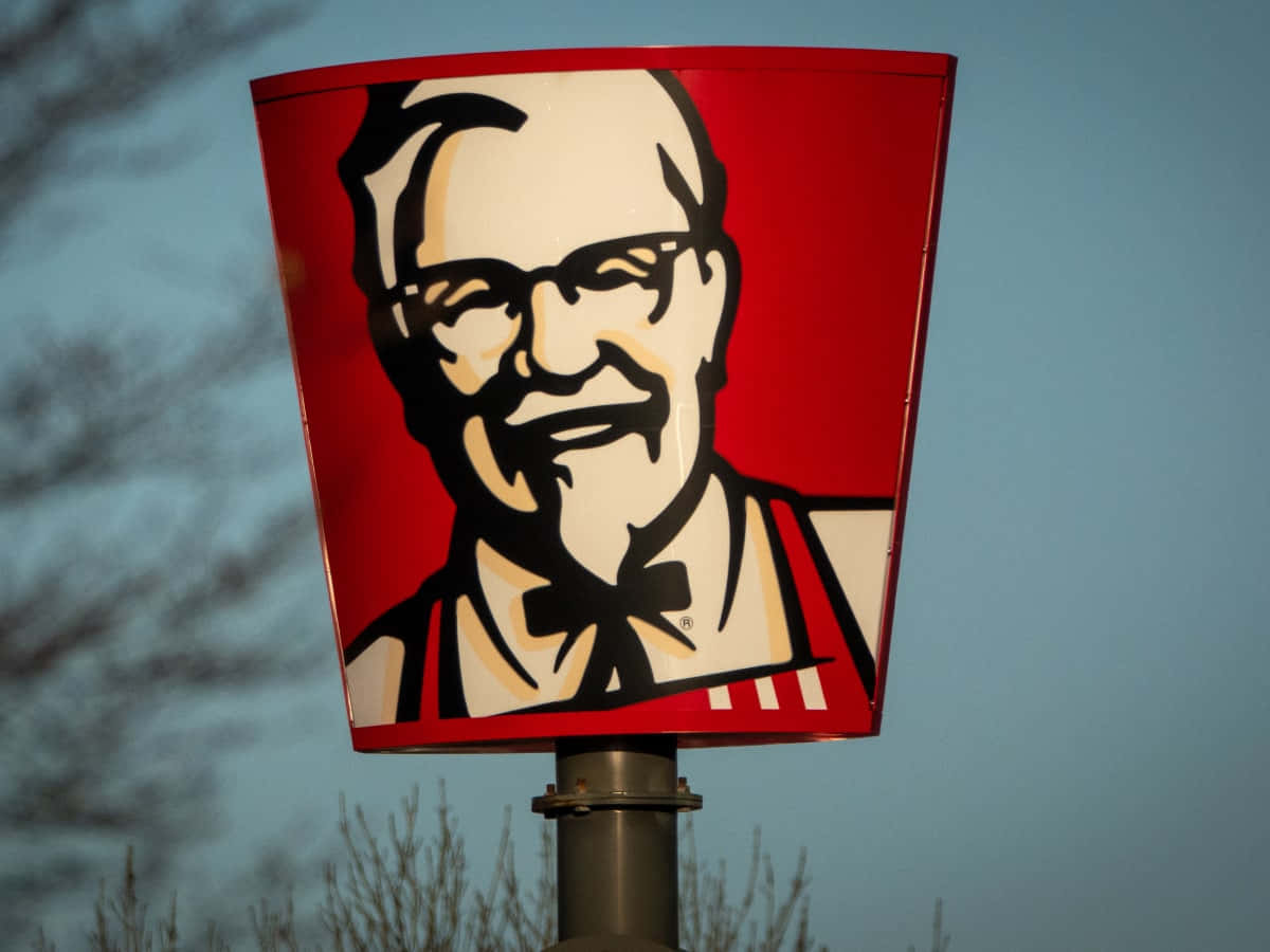 KFC桶形招牌，山德士上校臉孔，背景黃昏天空和光禿樹木。