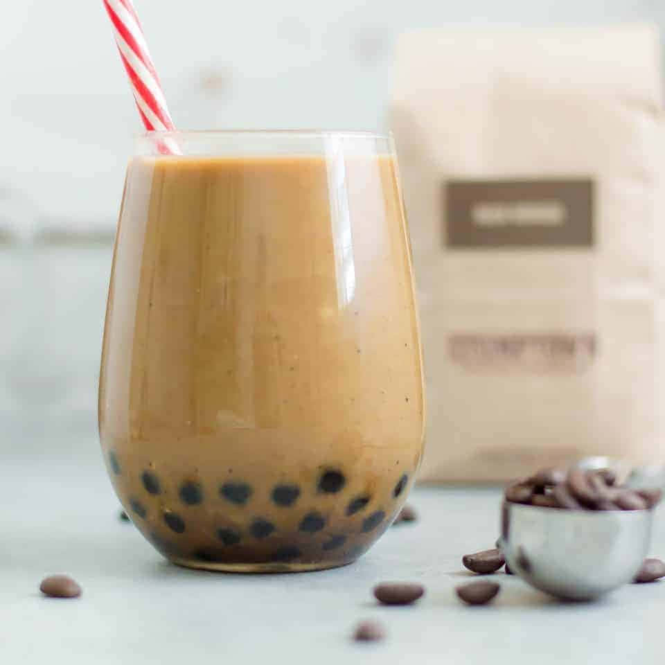 享受一杯美味的珍珠奶茶！ 壁紙 — 一杯奶油焦糖色的珍珠奶茶，內有黑色木薯珍珠，放在一個配有紅白間條飲管的玻璃杯中。