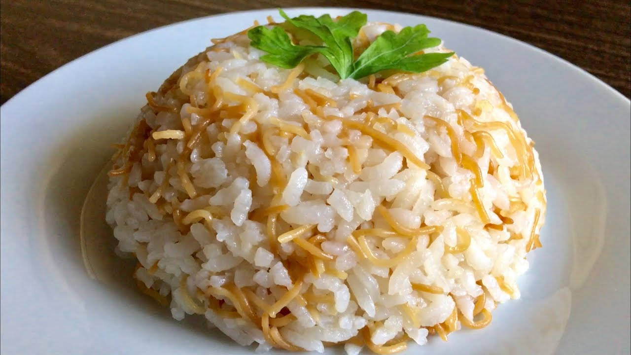 享受一碗豐盛的米線 壁紙 — 一團鬆軟白飯，上面放著金黃色炒麵和新鮮綠色歐芹葉，置於白色碟上。