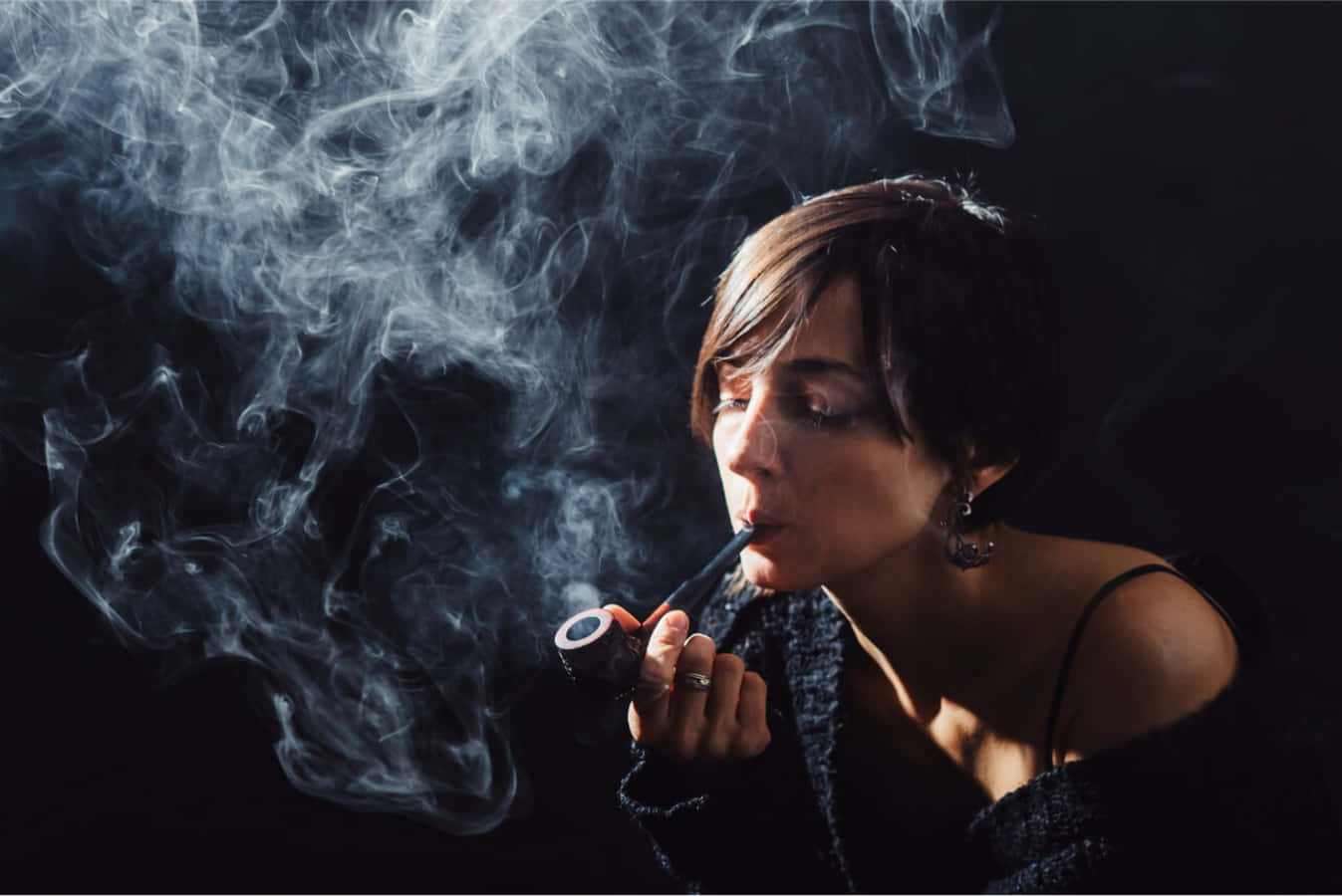 一位女性在深色背景前抽煙斗，煙霧旋轉。