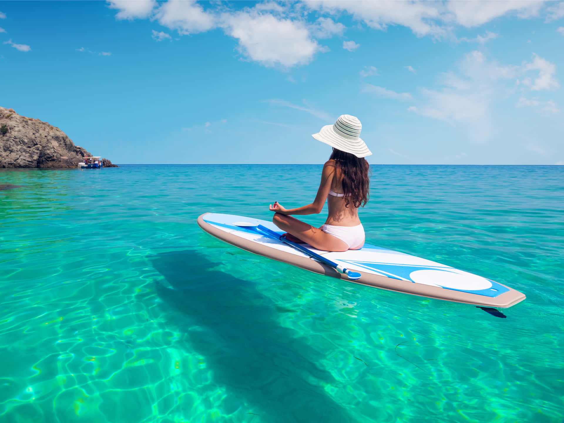 女士在清澈碧綠的海水中於槳板上冥想。