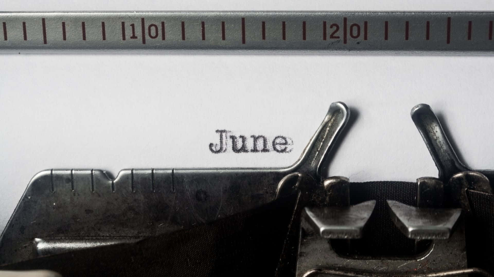 復古打字機喺白色紙上打出「June」一詞，上面有金屬尺。