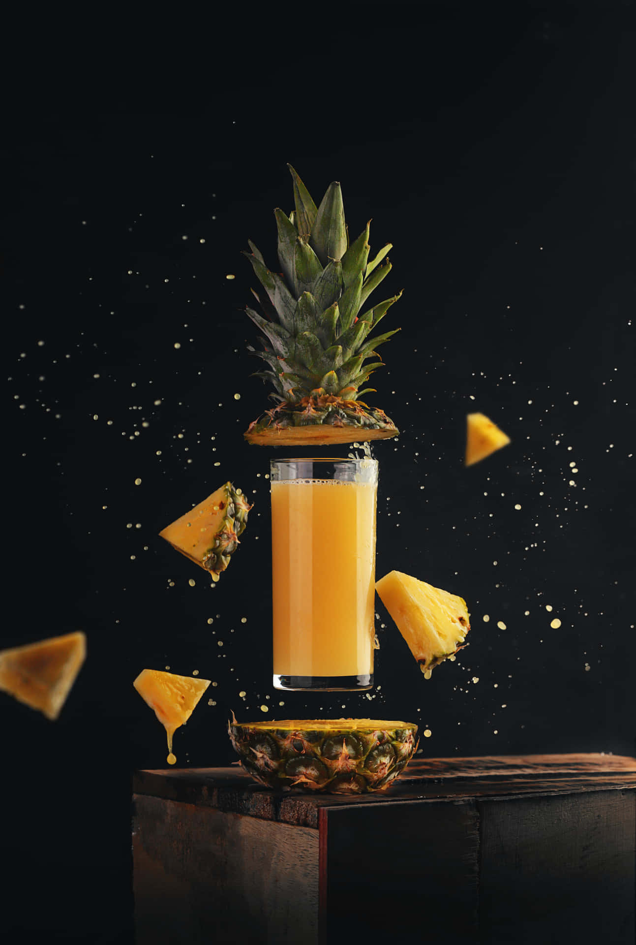 菠蘿汁杯，帶有漂浮的水果塊，置於深色木質表面上。