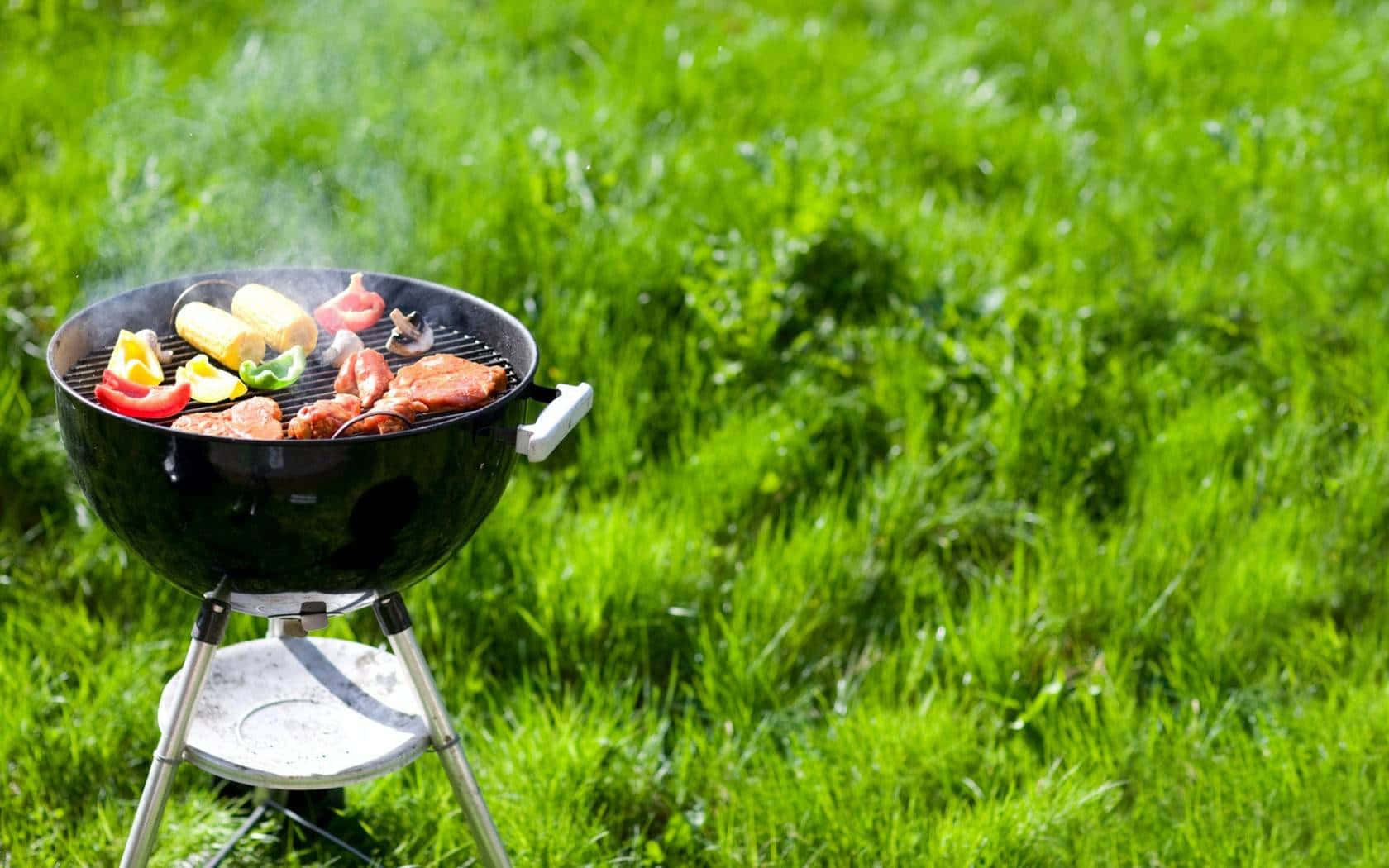 燒烤爐在綠色草地上，在明亮陽光下烹調肉、玉米和甜椒。