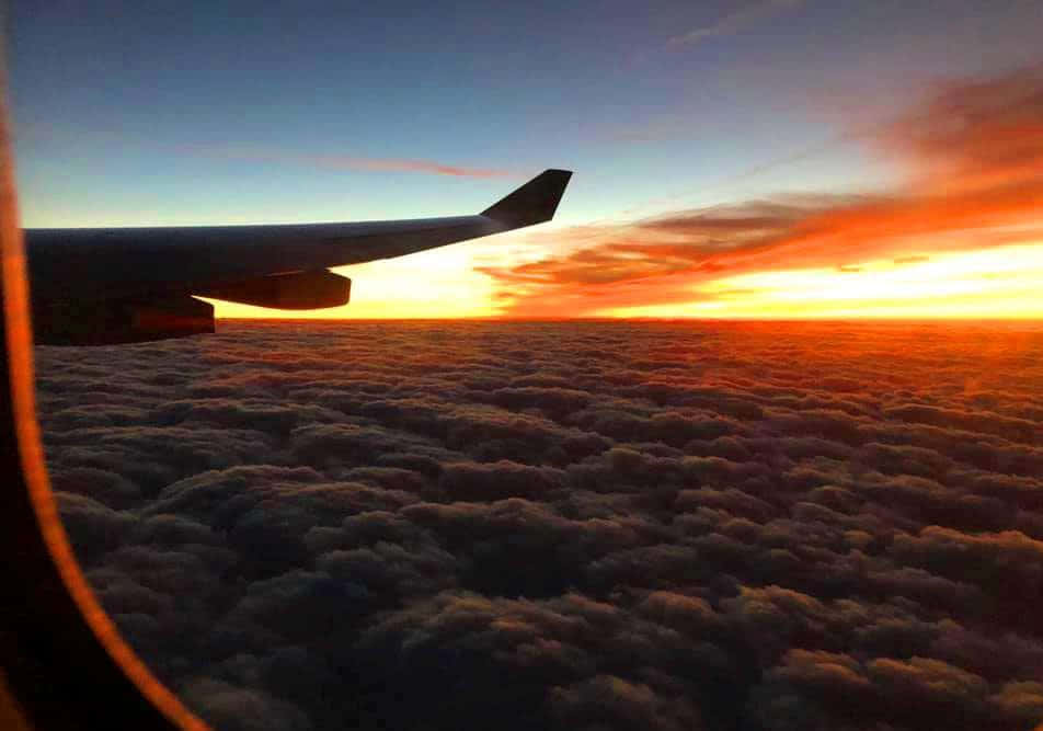 享受寒冷飛行 壁紙 — 飛機機翼在無盡棉花糖雲層之上，以火紅夕陽為背景形成剪影。