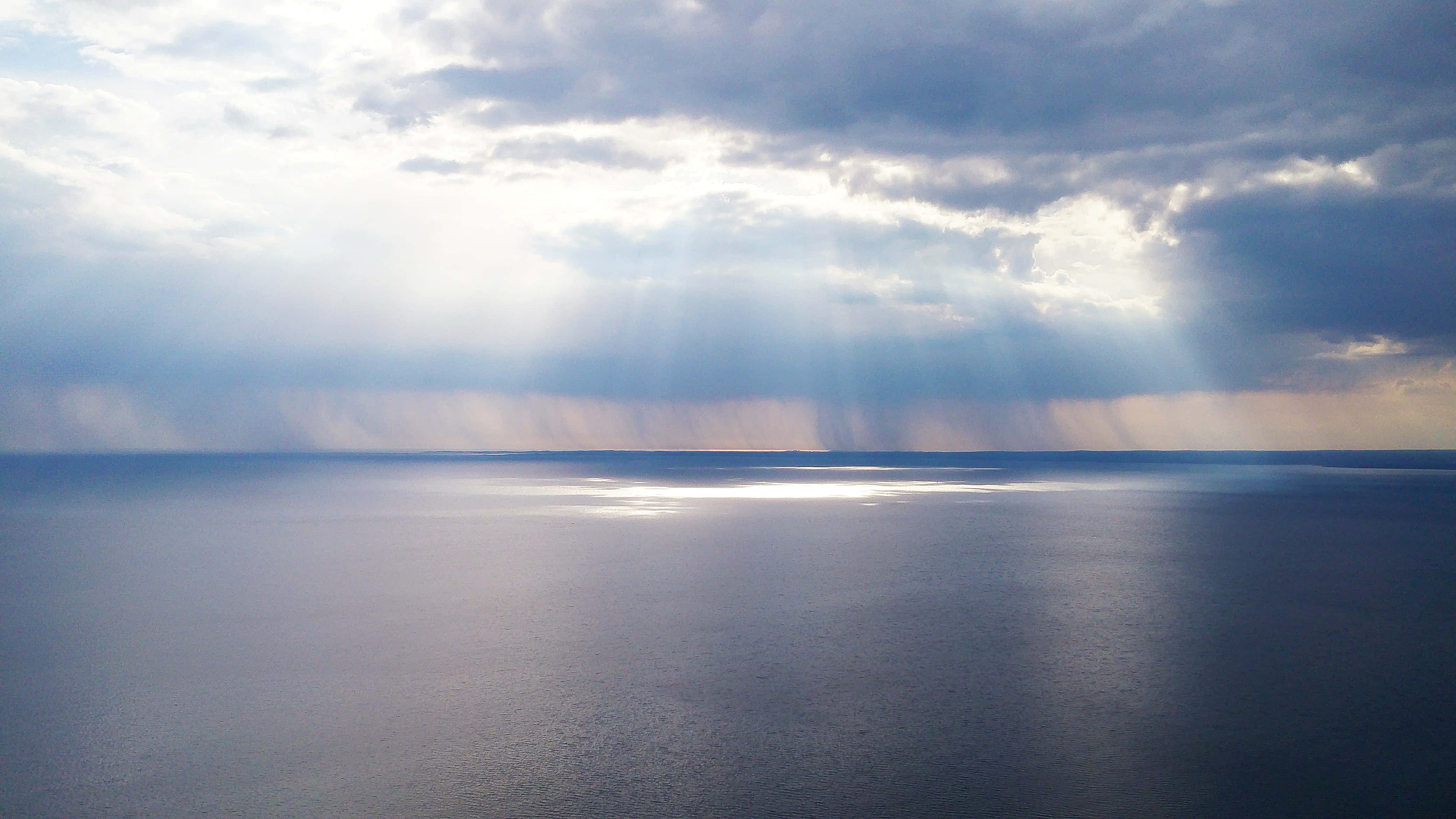 享受寧靜 壁紙 — 陽光穿透暴風雲層，在廣闊平靜的海洋地平線上投射出神聖的光芒。