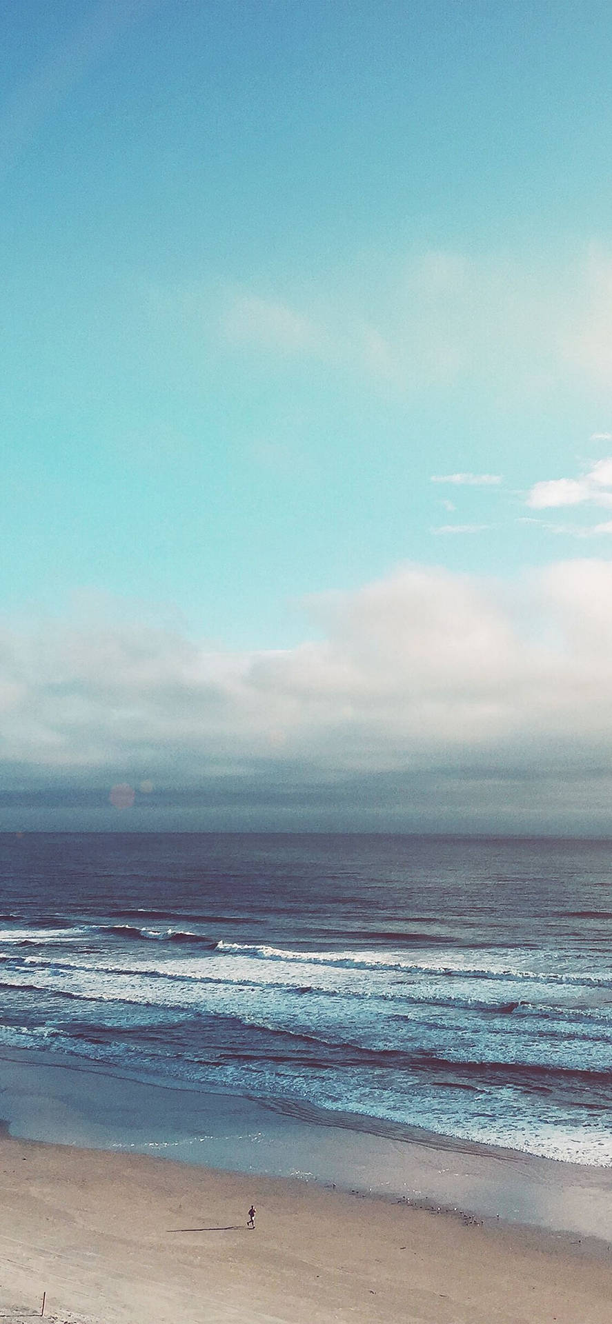 一個孤獨的人在海灘上行走，有海浪和多雲的天空。